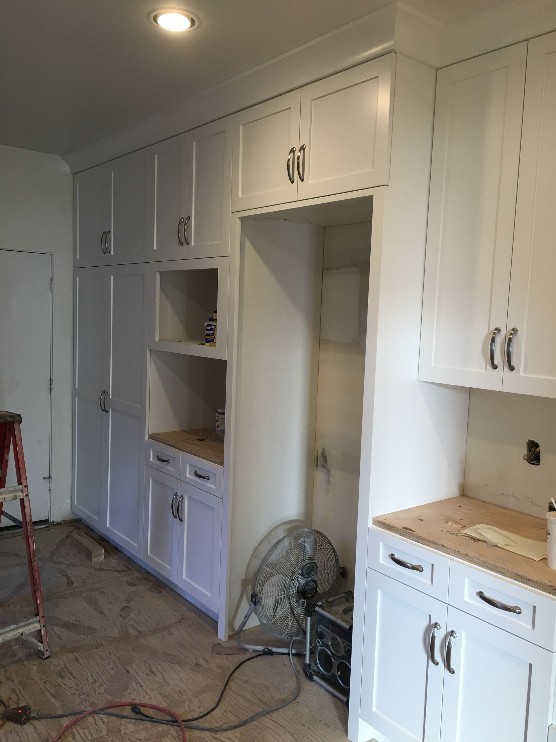 White kitchen cabinets under construction; empty refrigerator space.