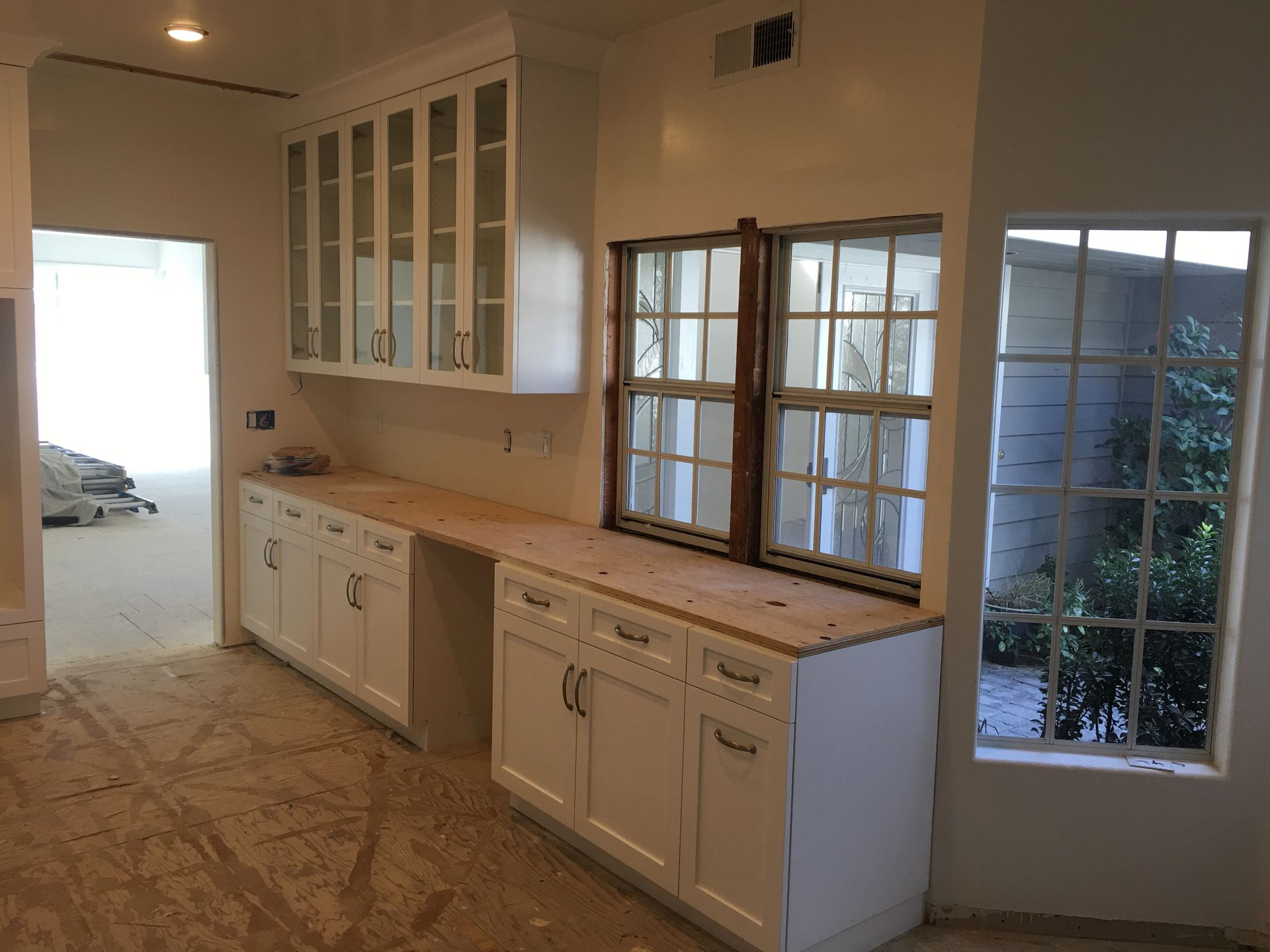 Kitchen remodel with white cabinets, wooden countertop, windows, and an unfinished floor.