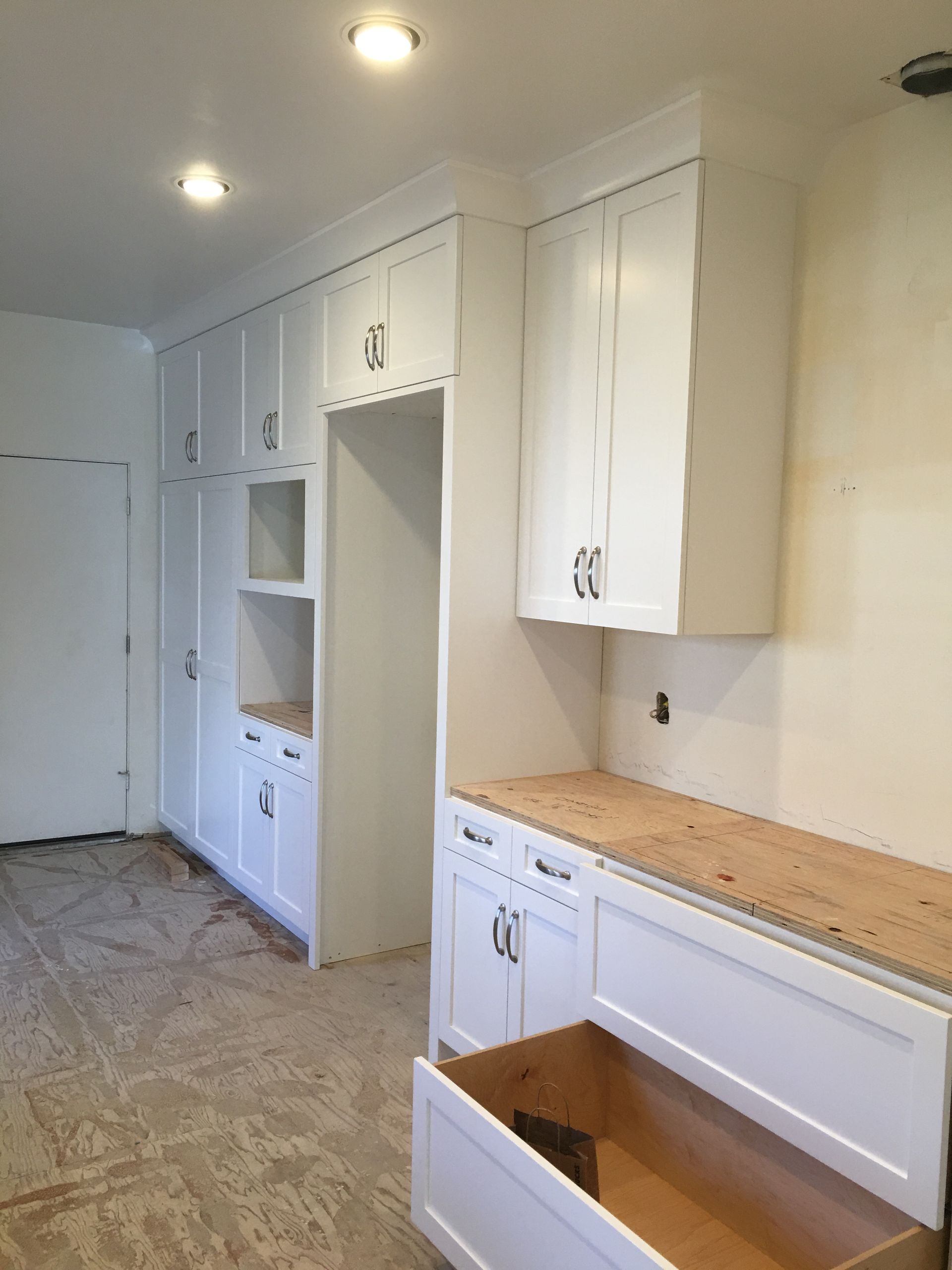 White kitchen cabinets with unfinished countertop and open drawer.