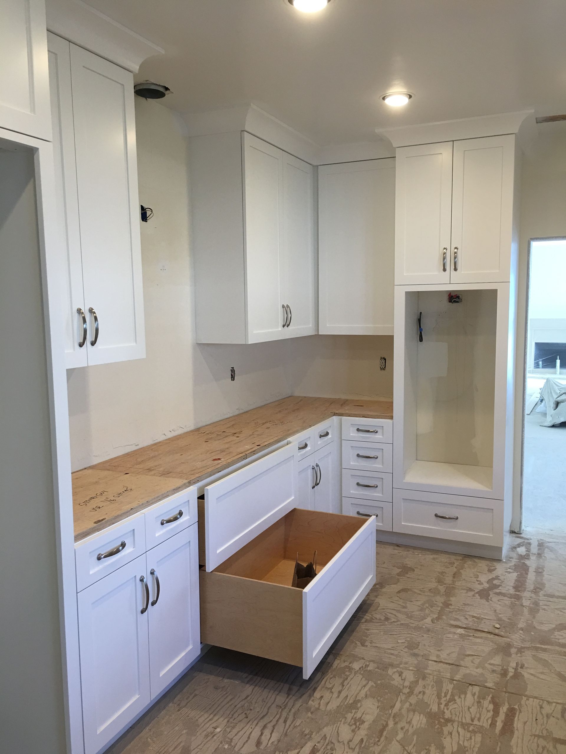 White kitchen cabinets with an open drawer, wooden countertop, and empty appliance niche.
