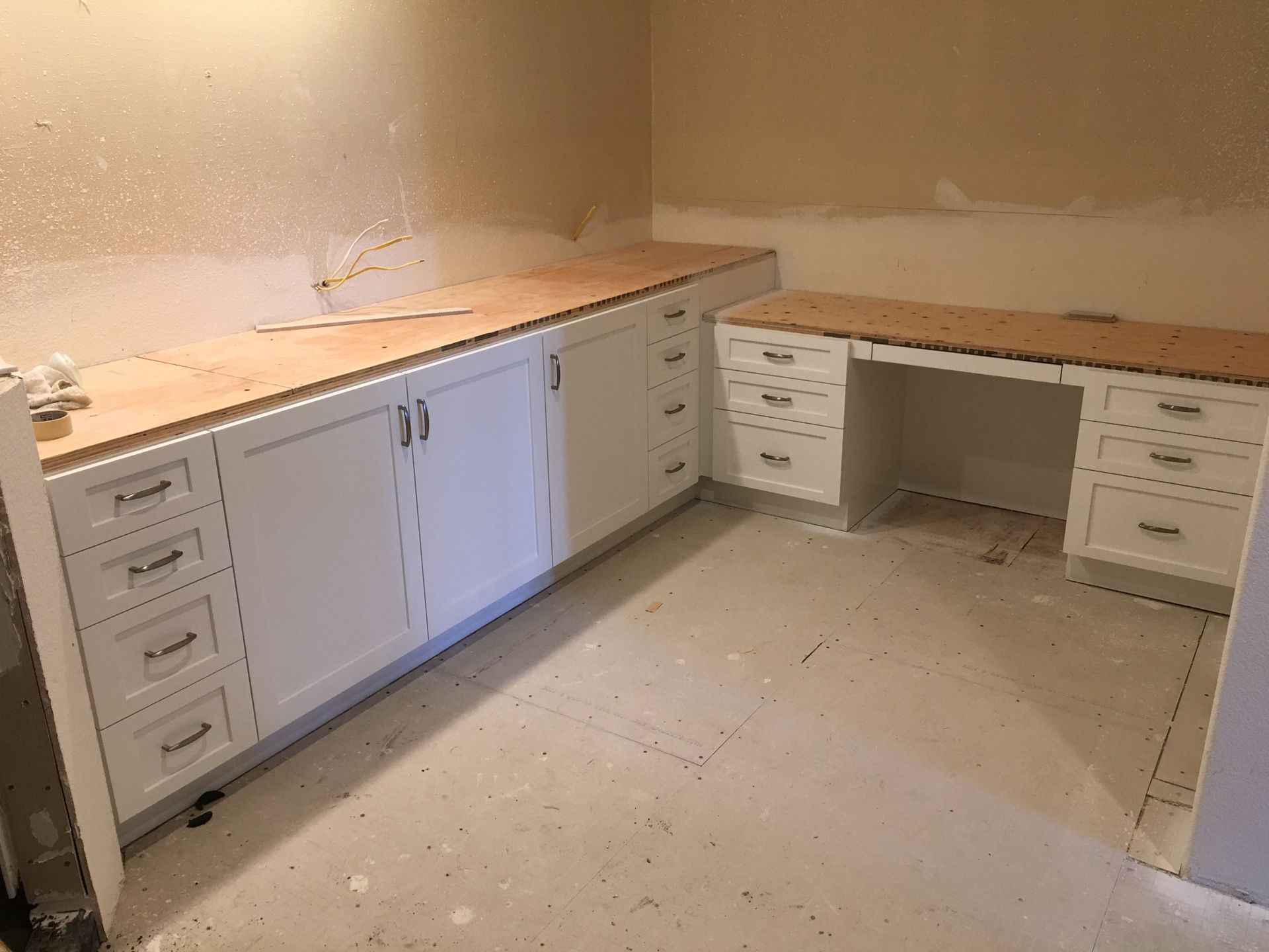 White cabinets with light wood countertops in a room under construction.