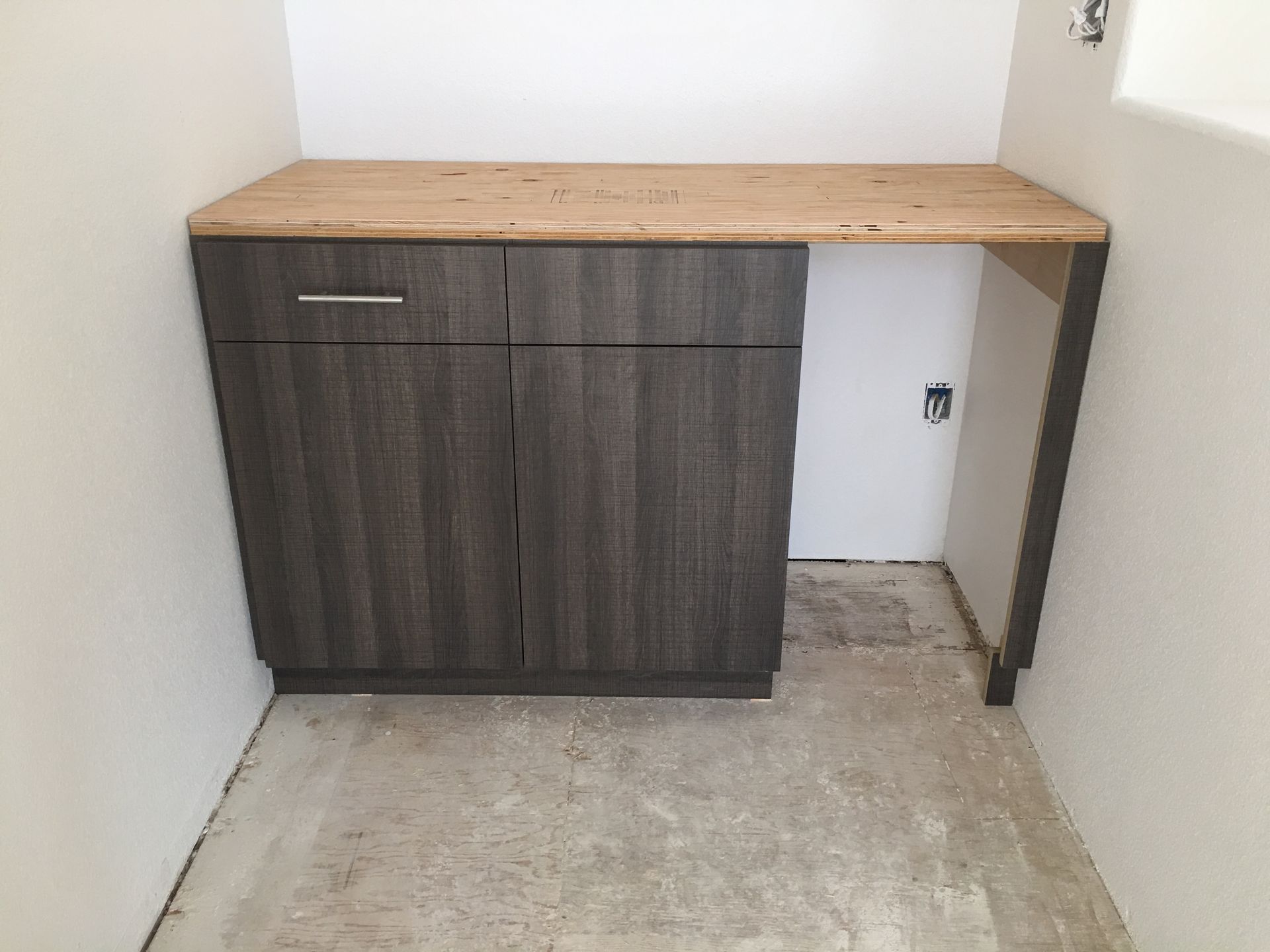 Dark gray cabinet with wood countertop in a small alcove.