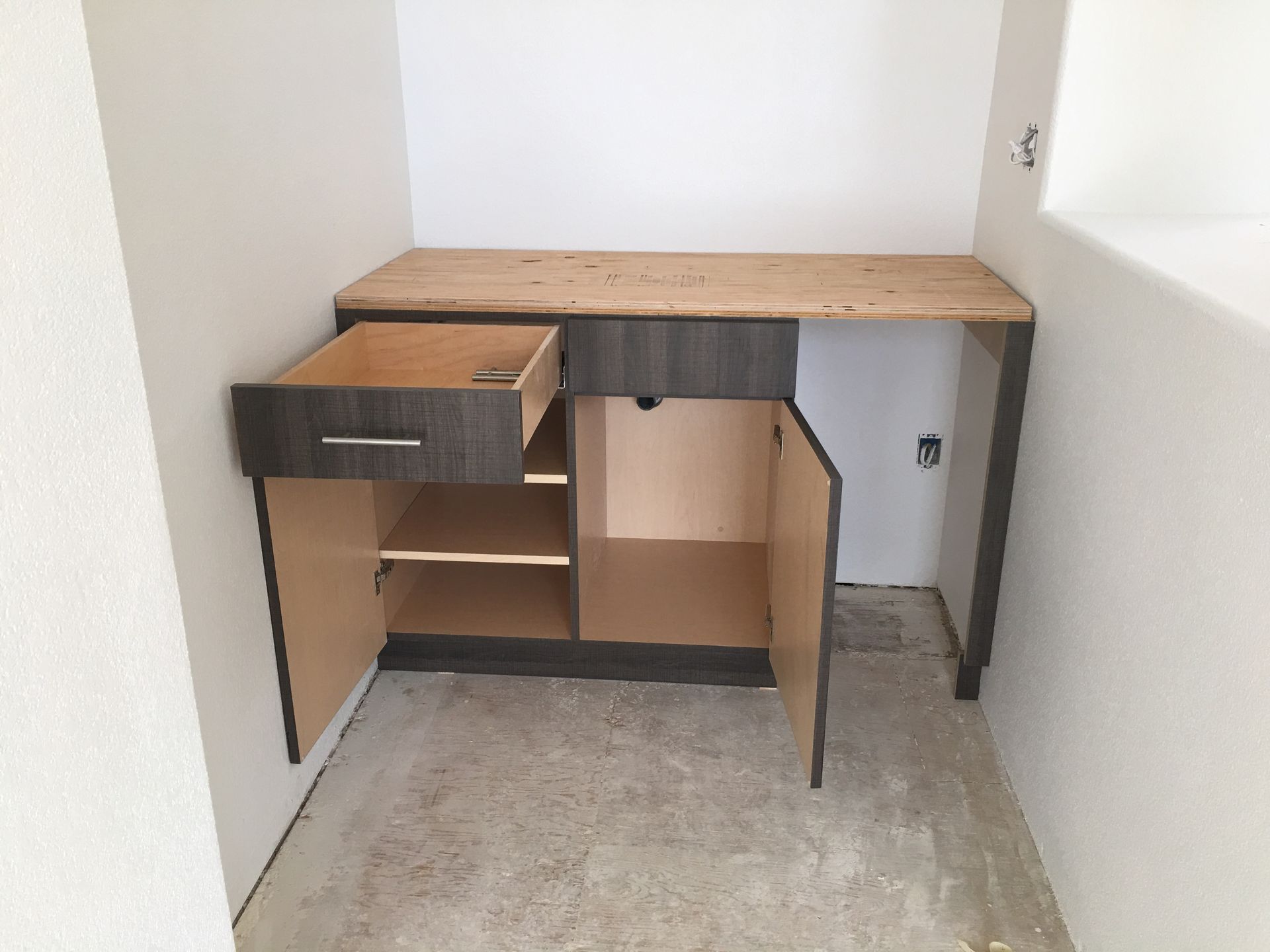 Dark wood cabinet with open drawer and door, light wood countertop, installed in a small alcove.