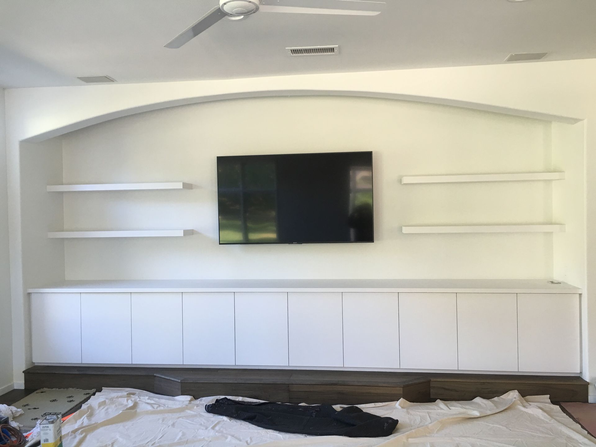 White built-in entertainment center with shelves, TV, and cabinets, in a room with a light fixture and flooring.