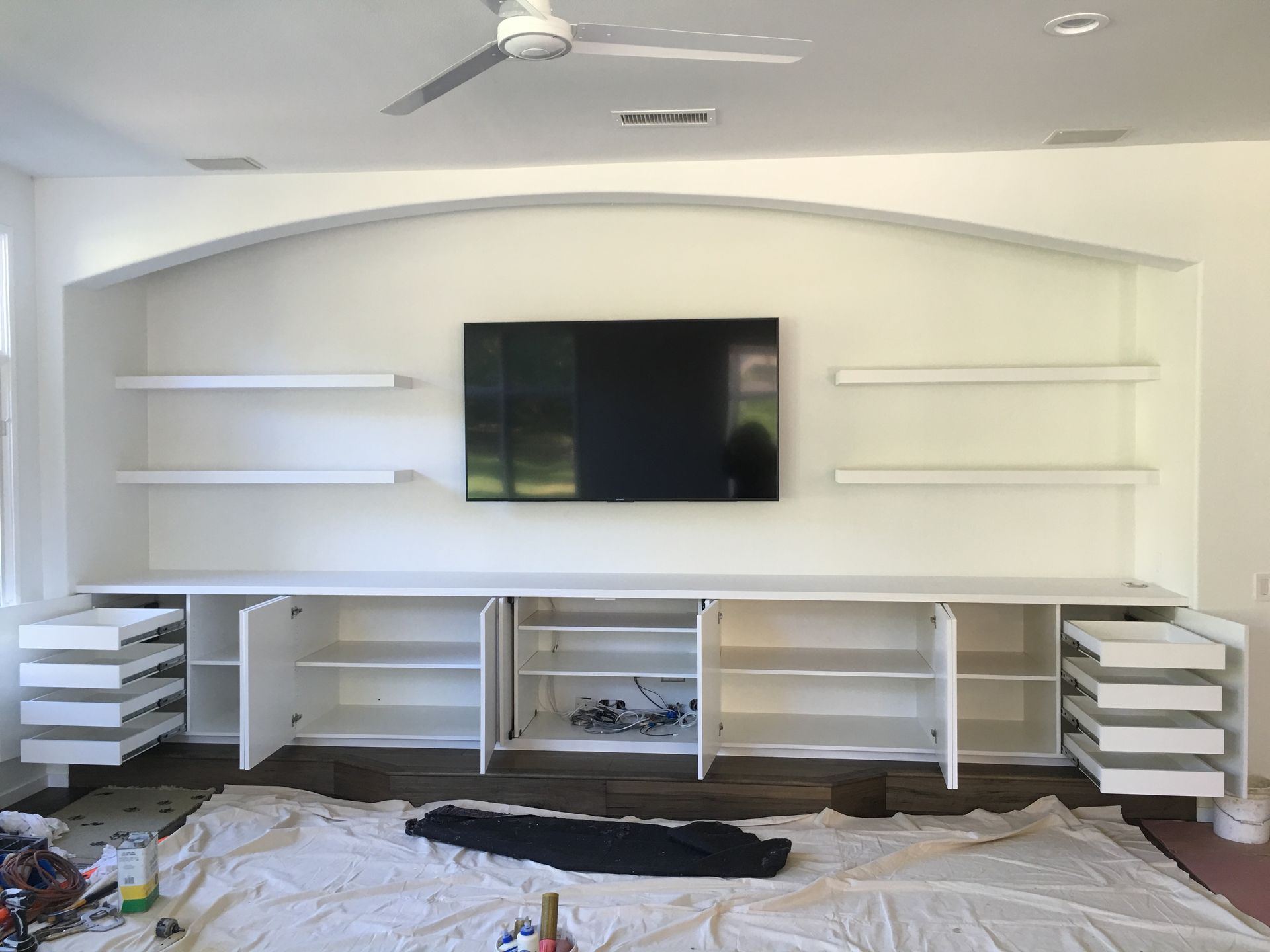 Built-in white entertainment center with cabinets, drawers, shelves, and a TV; room is being renovated.