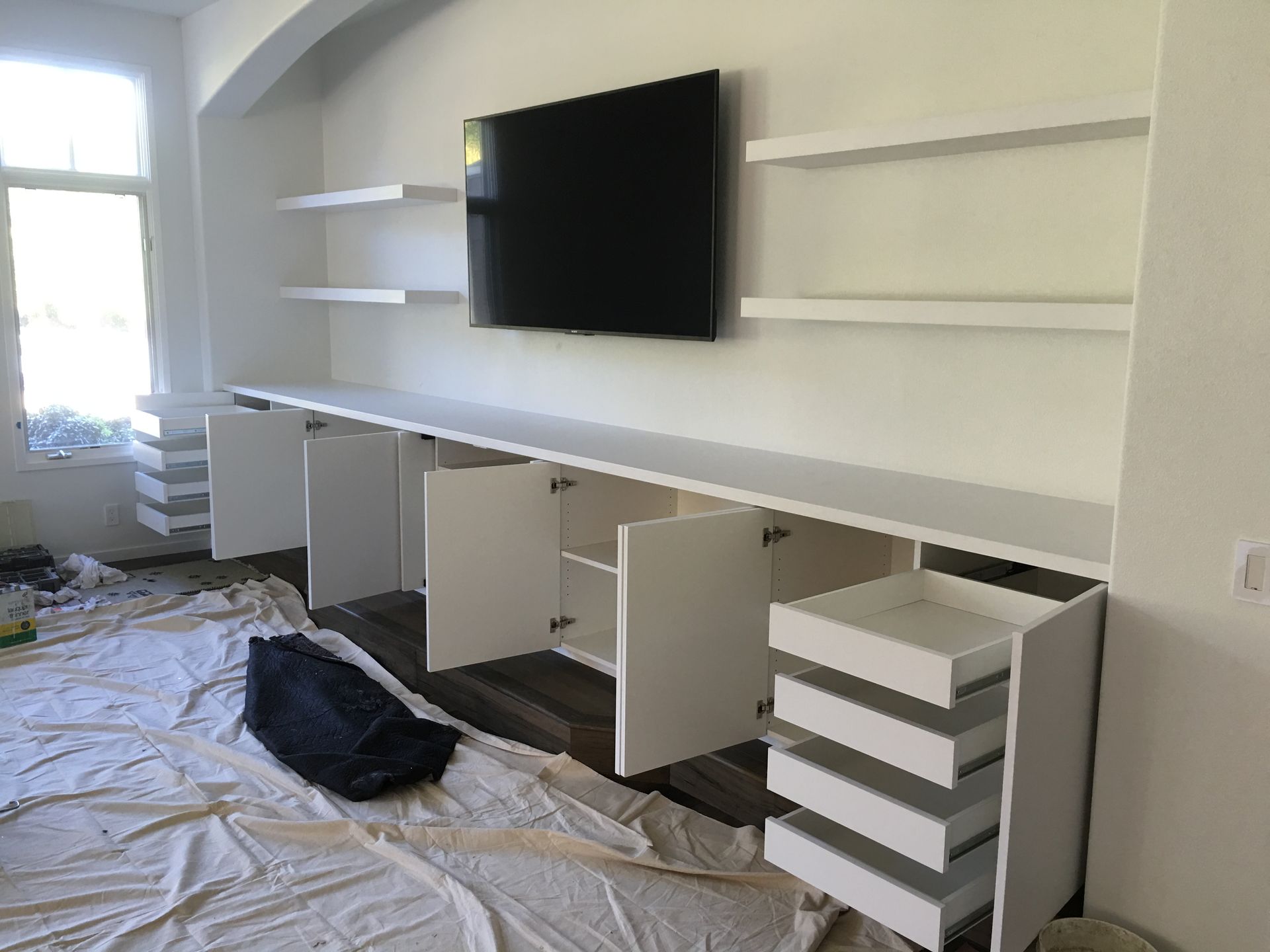 Built-in white media center with TV, shelves, cabinets, and drawers in a room, still under construction.