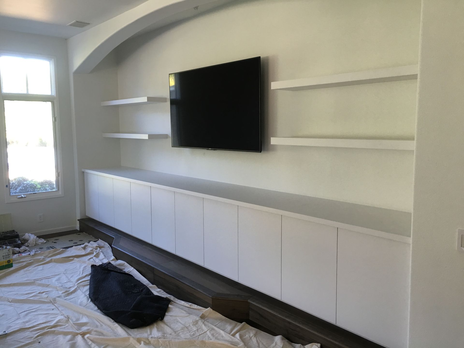 White built-in wall unit with shelves and cabinet doors, centered around a mounted TV.