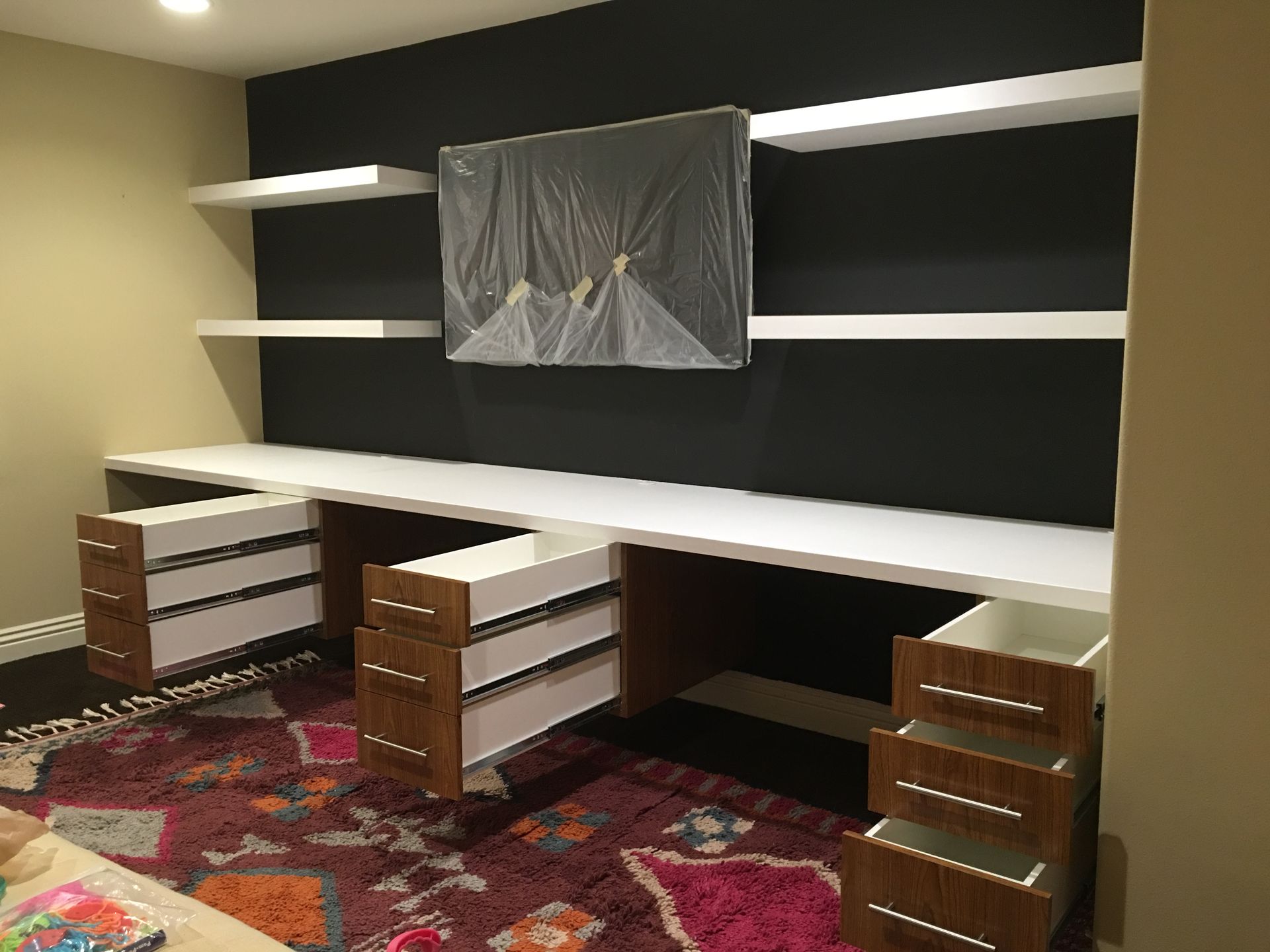 Built-in office with a black accent wall, white shelves, and a large white desk with open drawers.