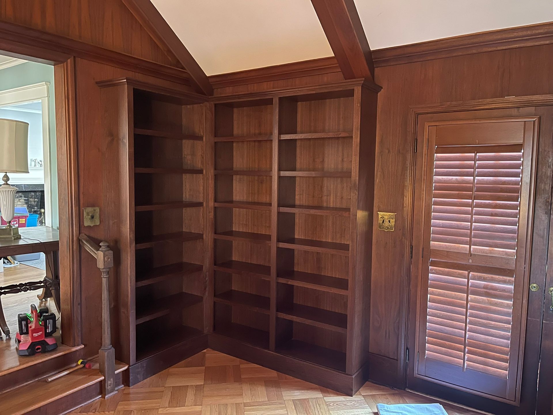Wooden built-in bookshelves in a room with wood paneling and a doorway with shutters.