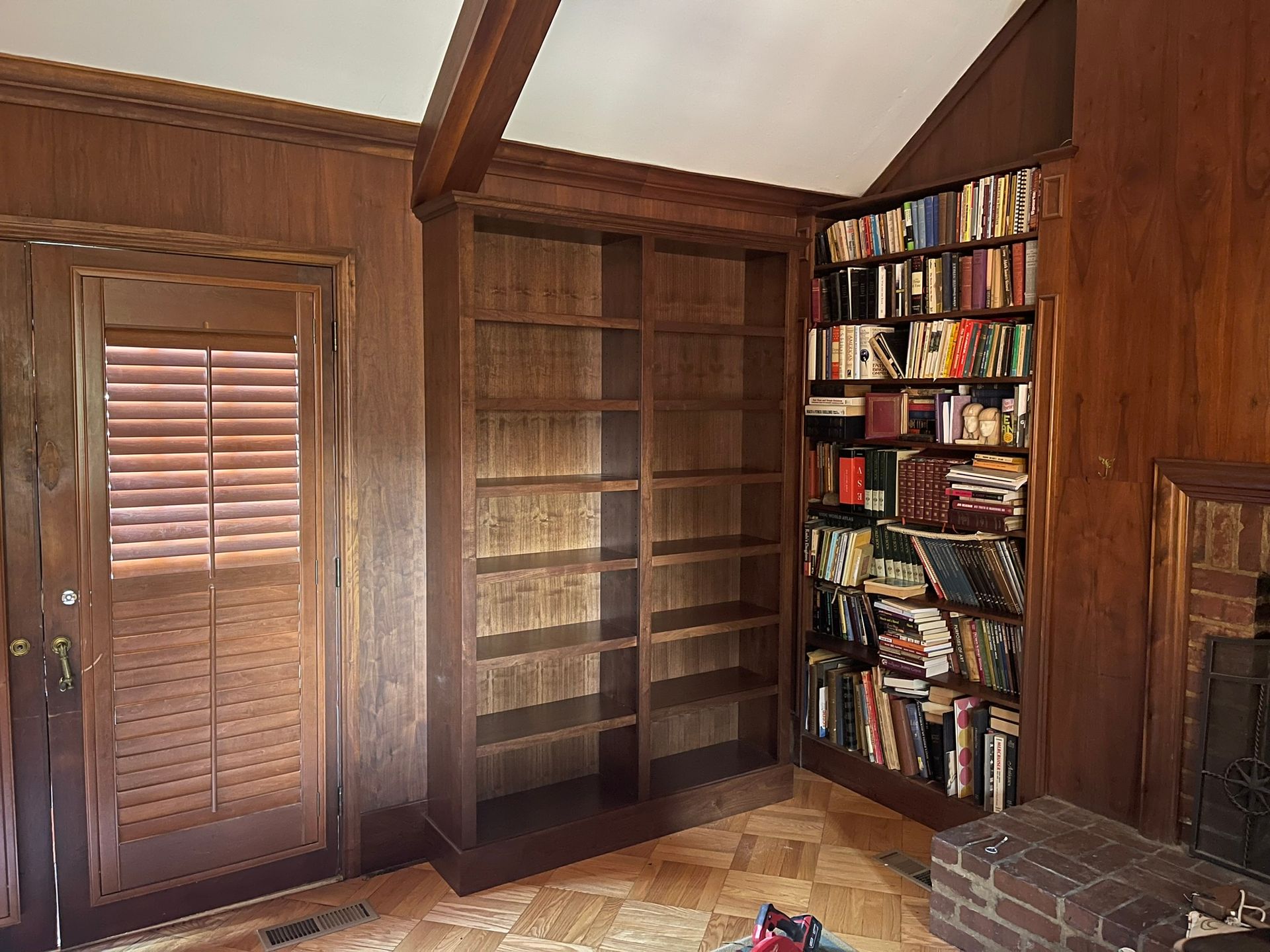 Wooden bookshelves filled with books and empty shelves, next to a door and fireplace.