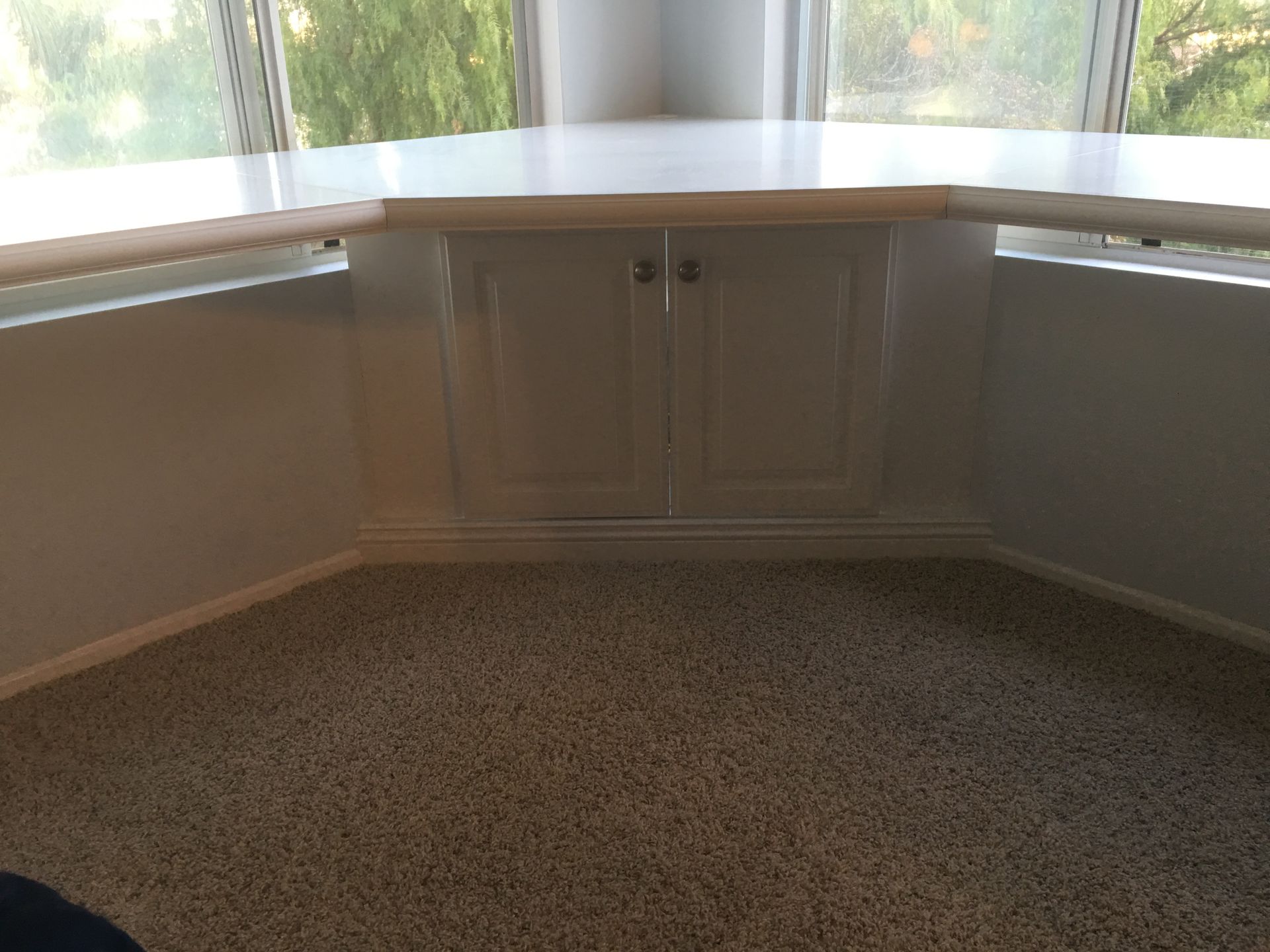 White cabinet under a window in a corner, with a countertop and beige carpet.