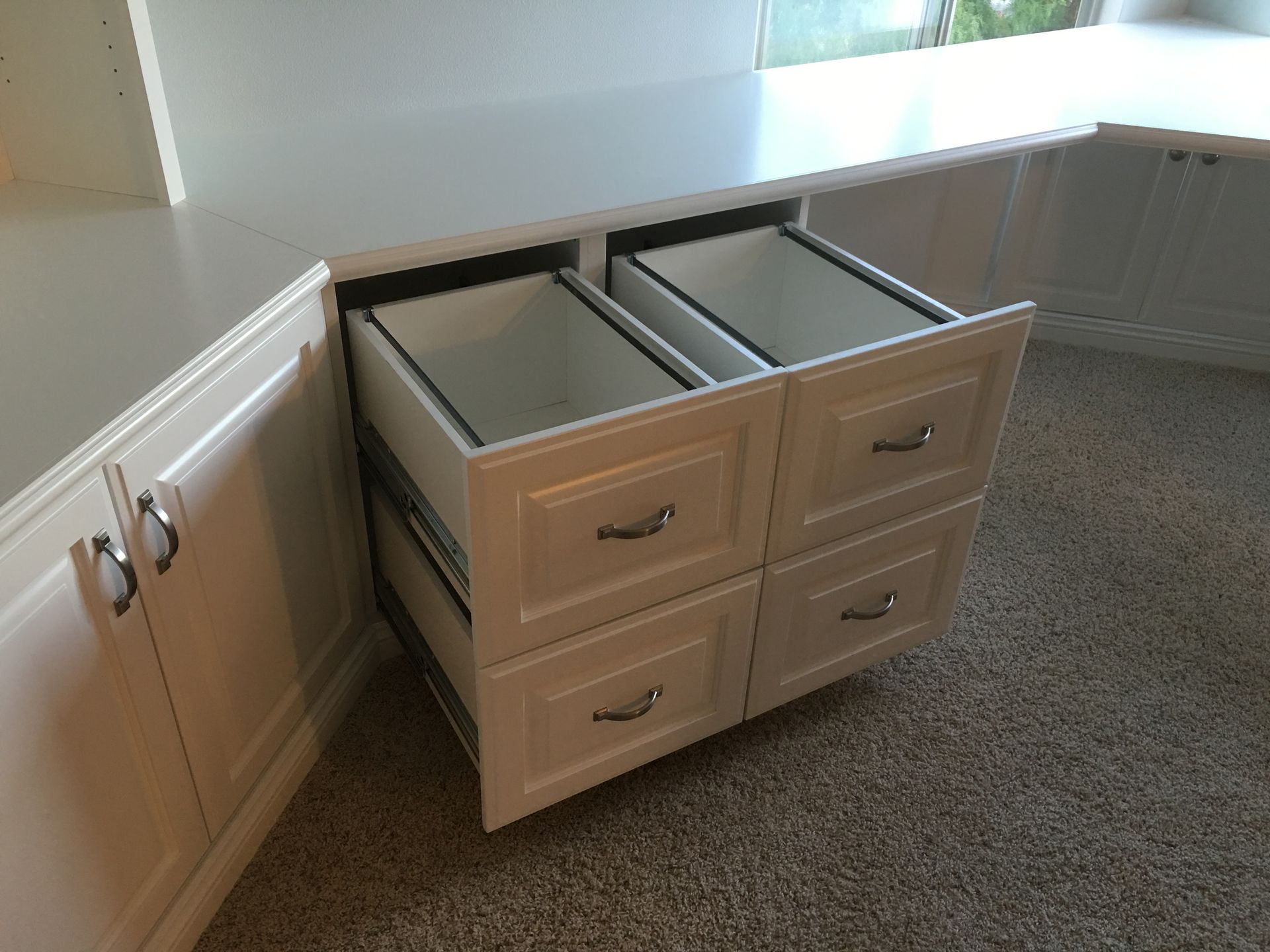 White built-in cabinet with two open pull-out trash bins, sitting on a carpeted floor.