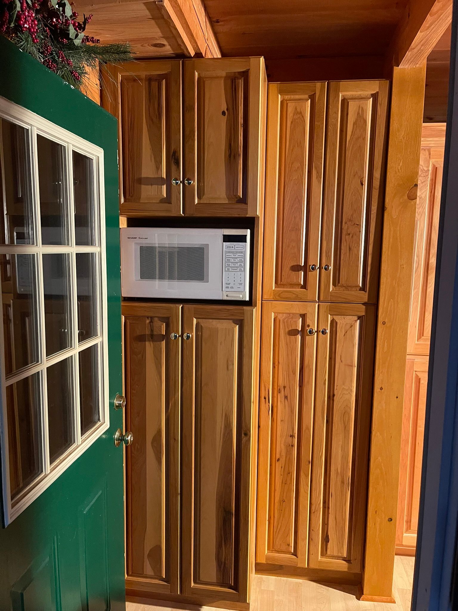 Green door opens to wooden cabinets with a microwave.