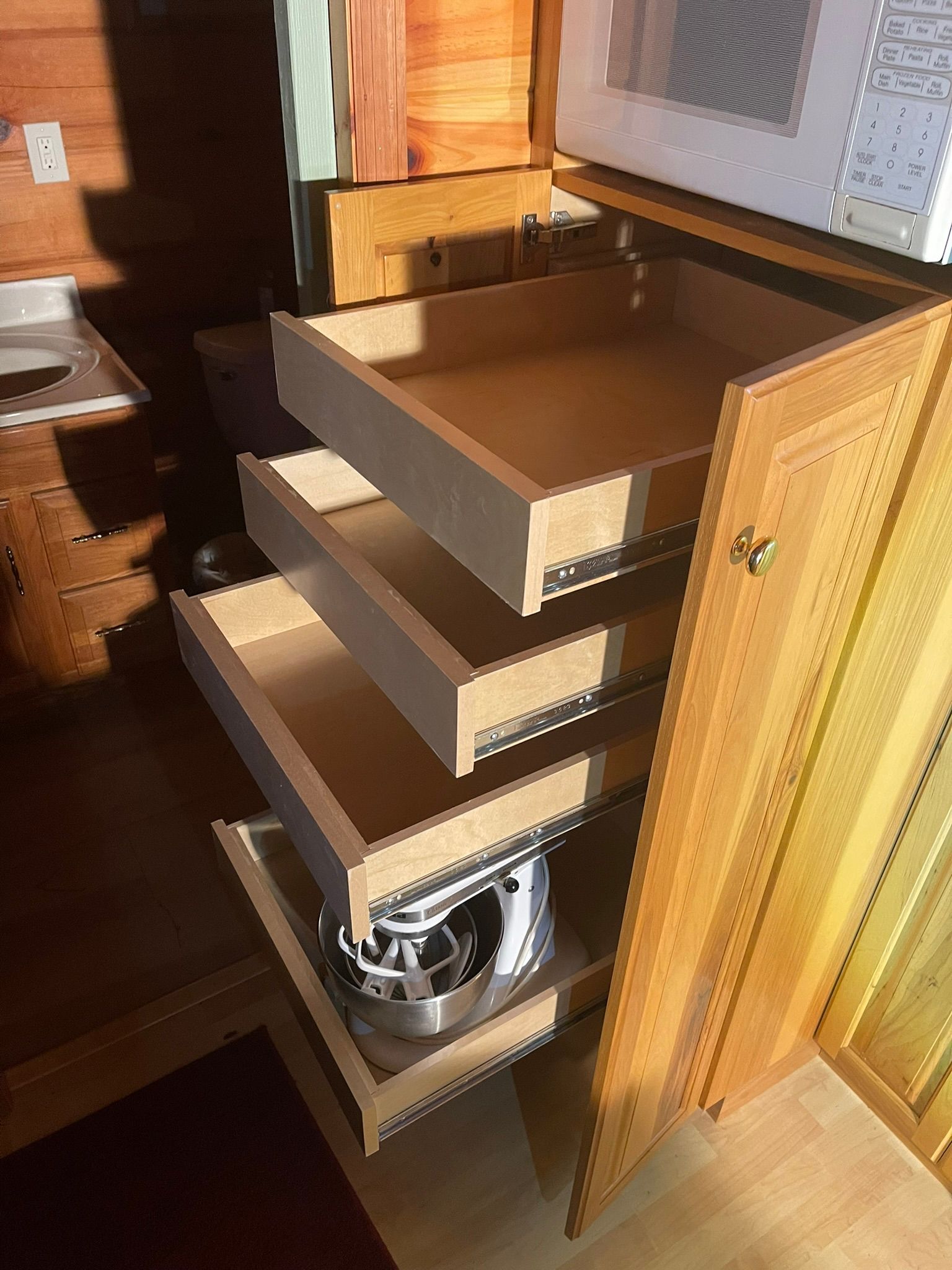 Wooden kitchen cabinet with three open drawers, holding a pot in the bottom drawer.