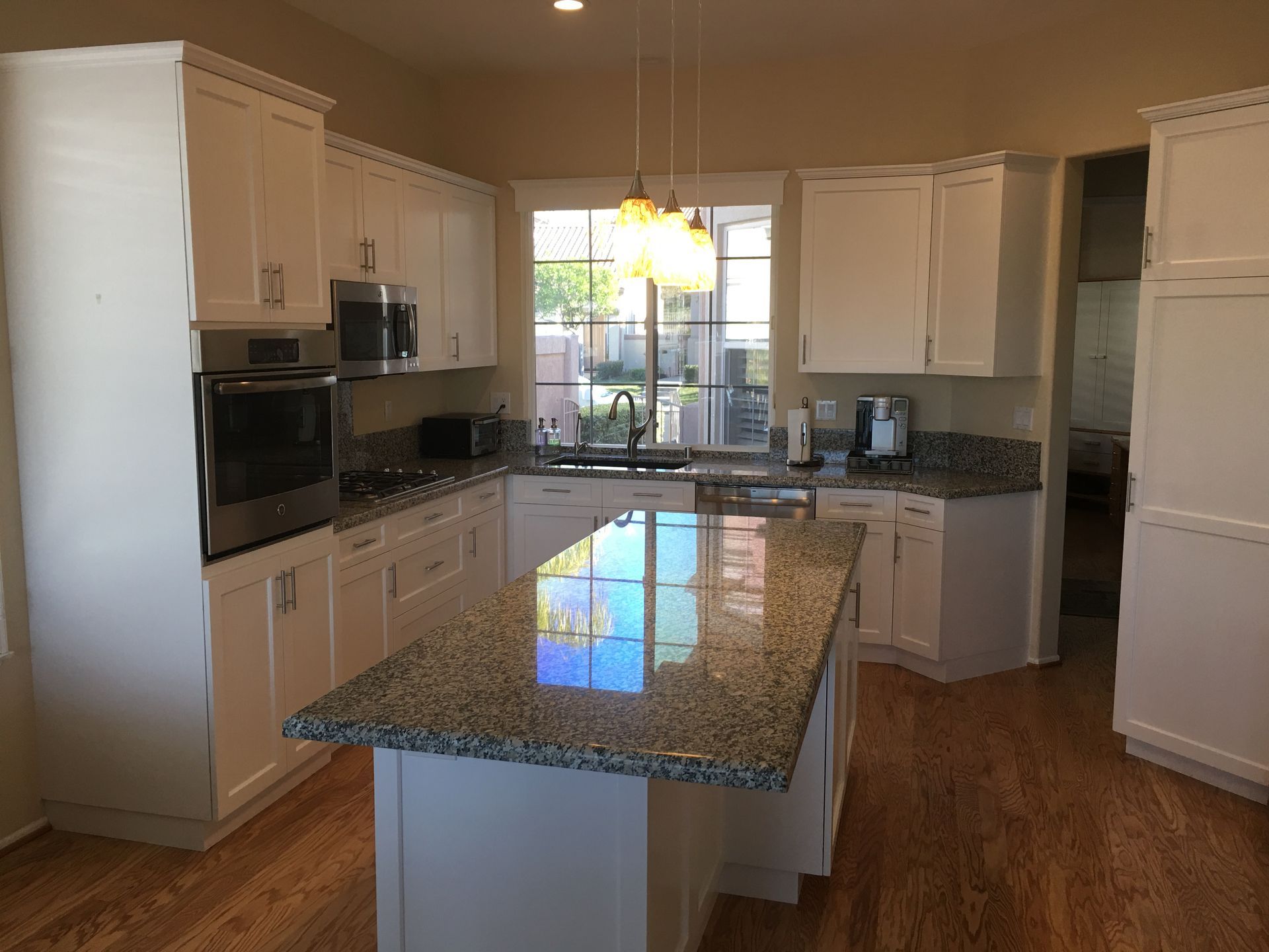 White kitchen with granite countertops, island, and wood floors.