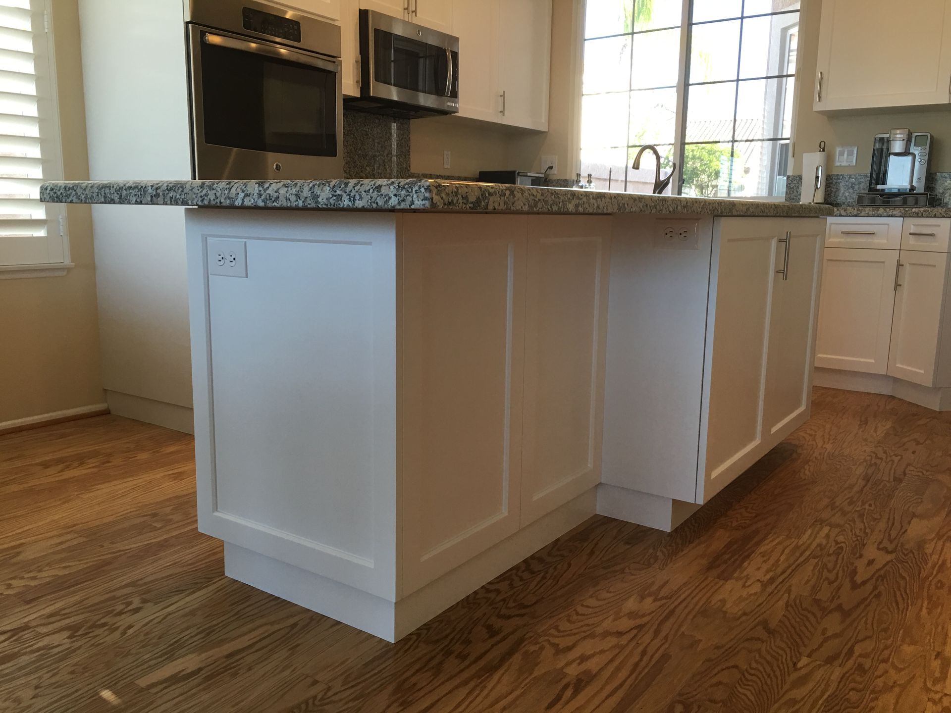 White kitchen island with granite countertop, wooden floor, and a built-in outlet.