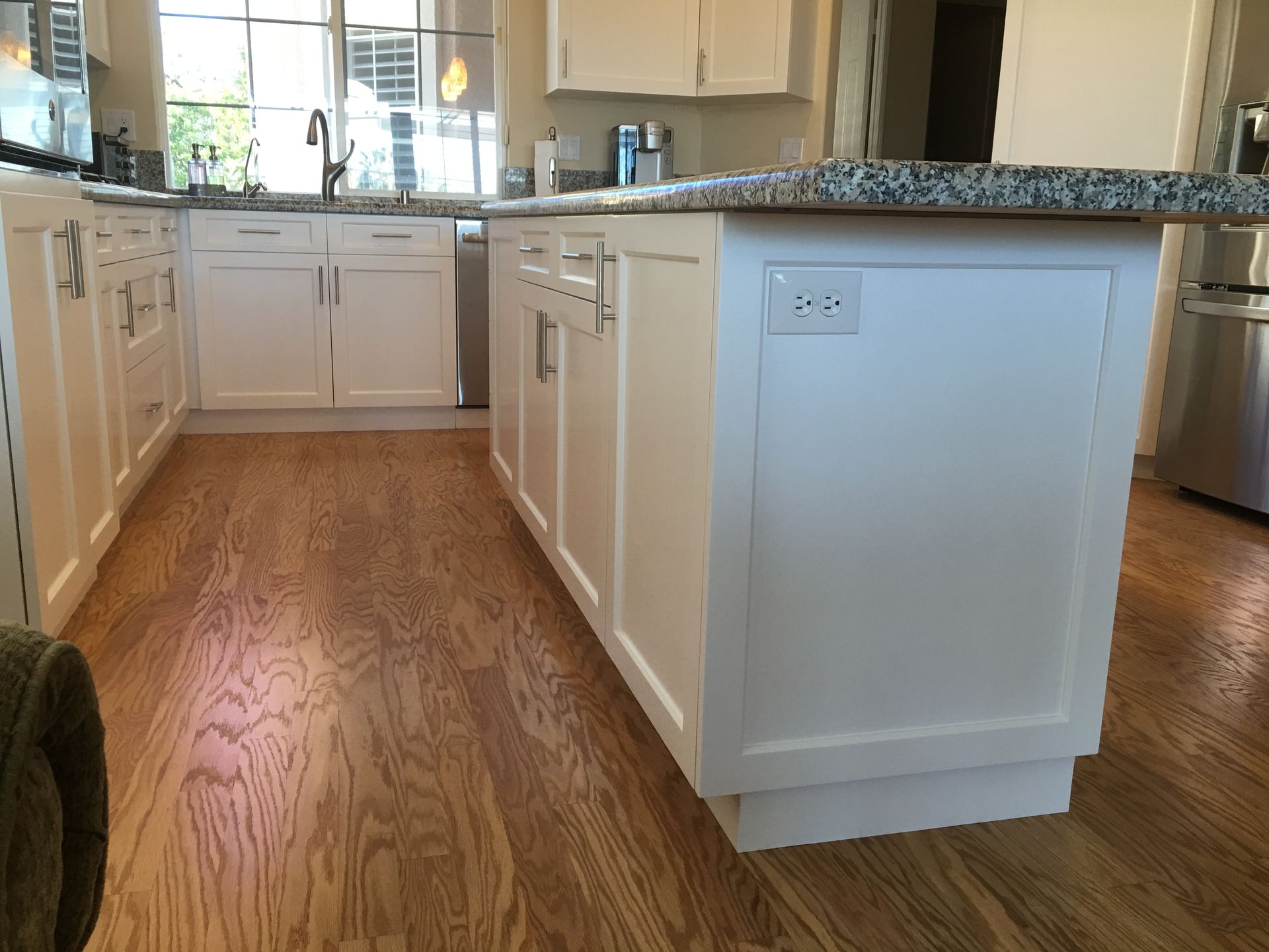 White kitchen with hardwood floors, a kitchen island, and granite countertops.