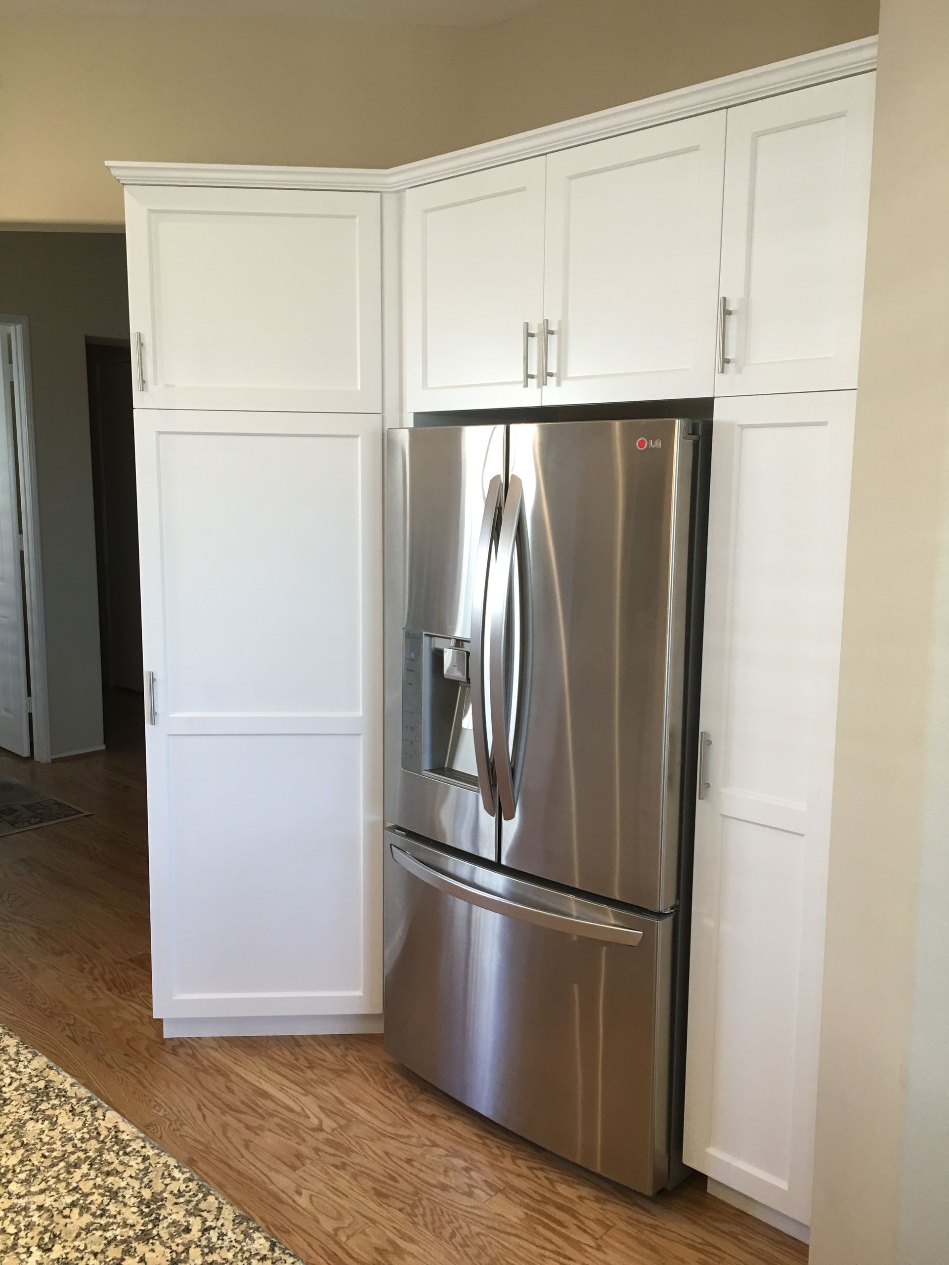 White kitchen cabinets surround a stainless steel refrigerator on wood flooring.