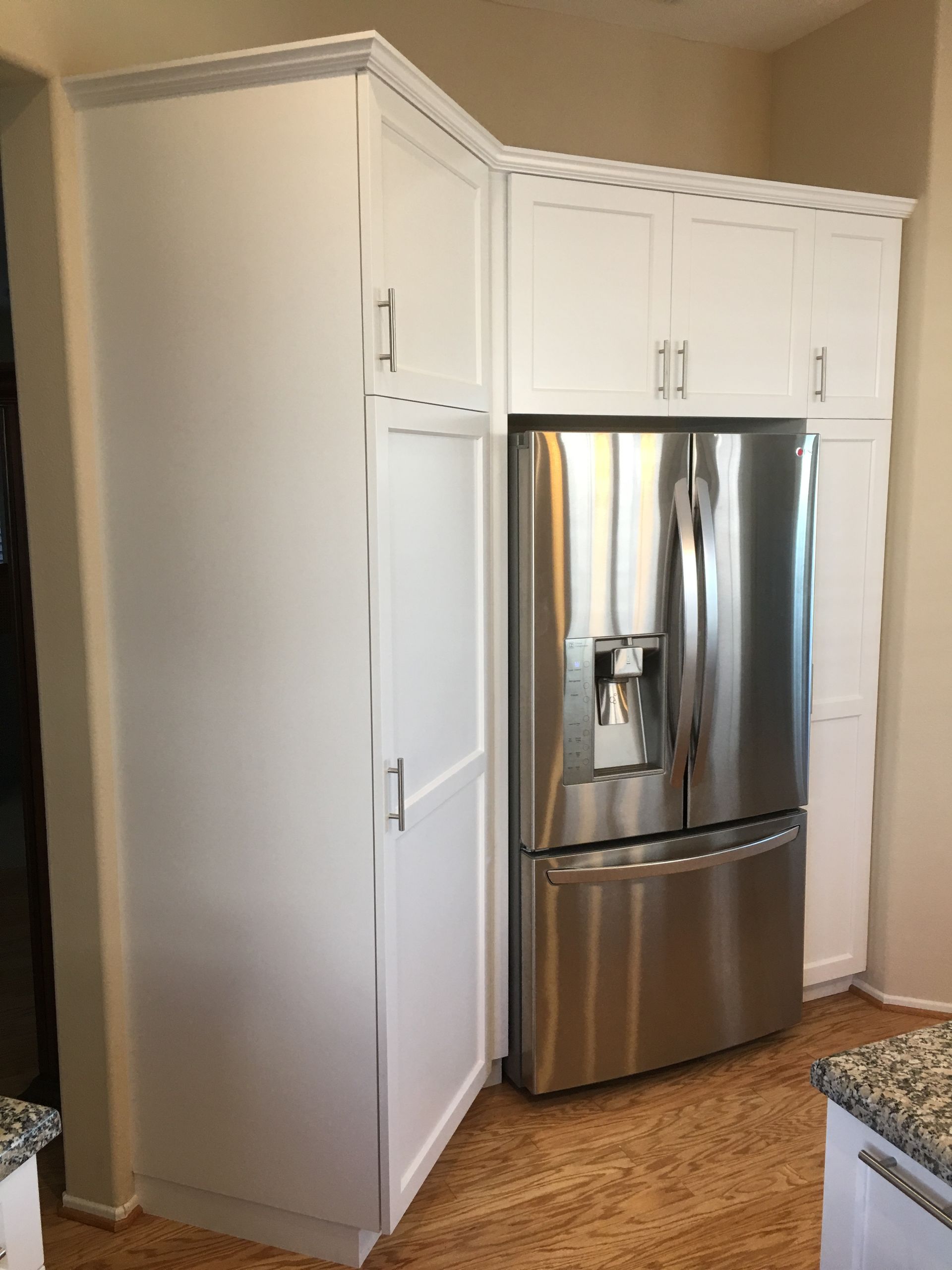 White kitchen cabinets surround a stainless steel refrigerator in a corner.