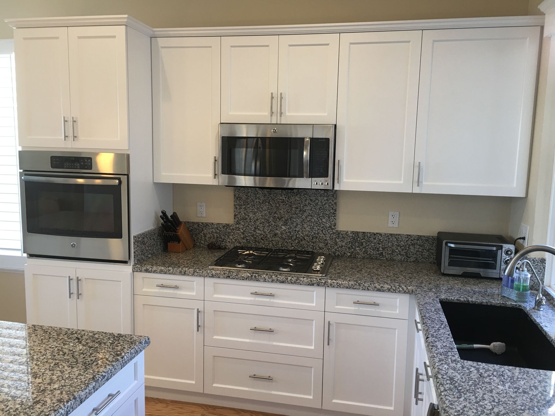 White kitchen cabinets with granite countertops, oven, microwave, and cooktop.