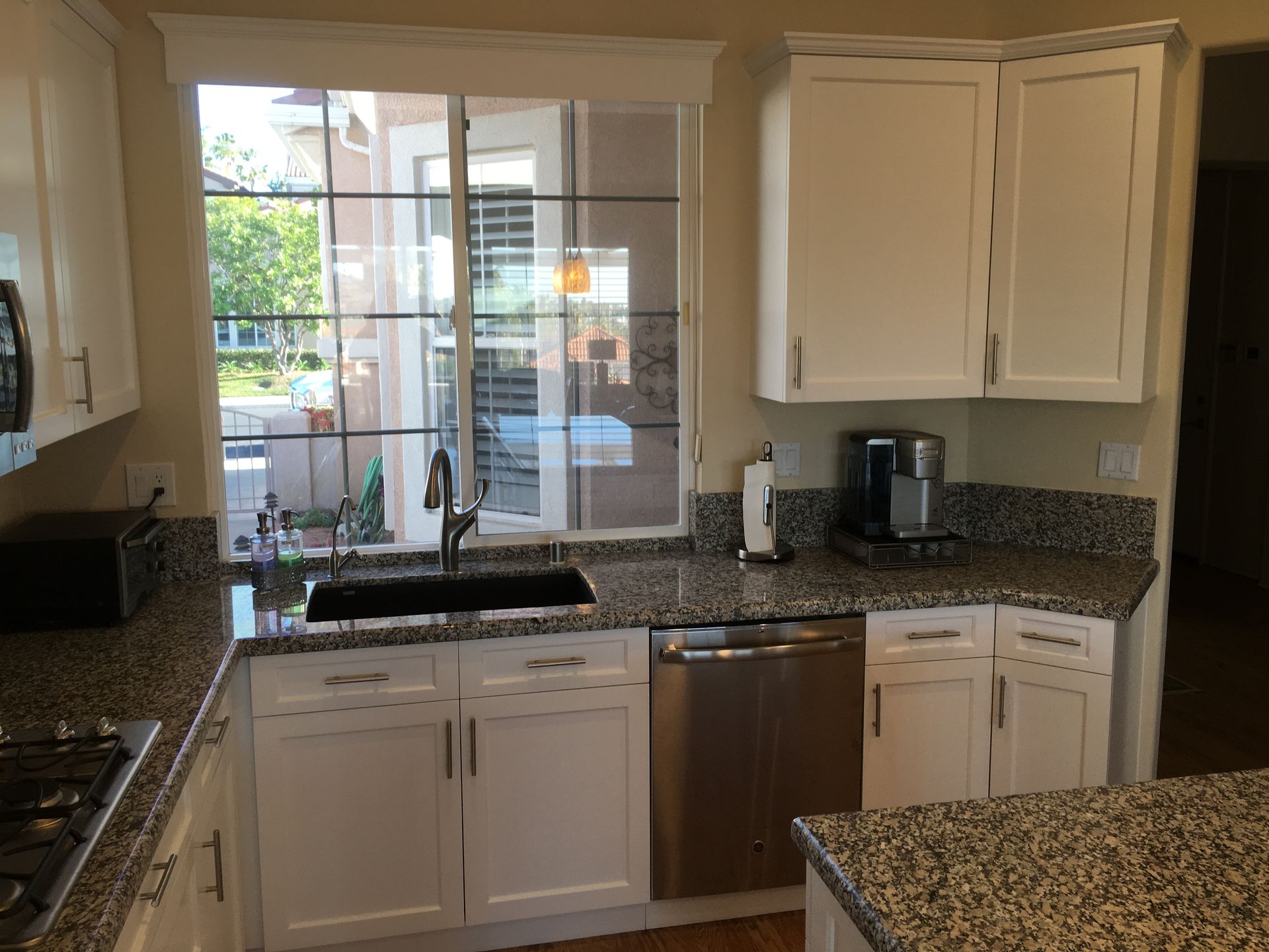 White kitchen with granite countertops, stainless steel appliances, and a window overlooking an outdoor patio.