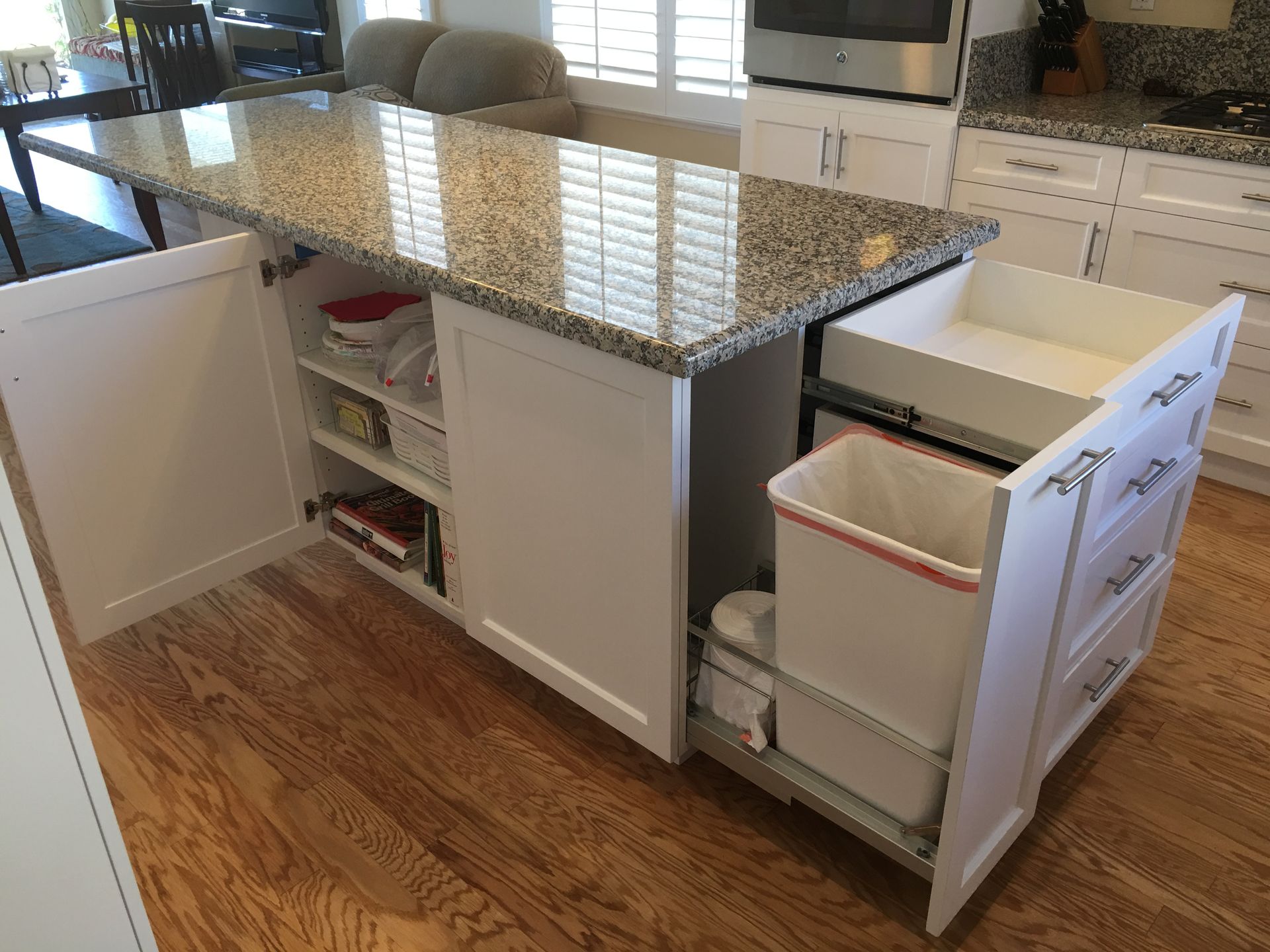 White kitchen island with granite countertop, cabinet doors open. 