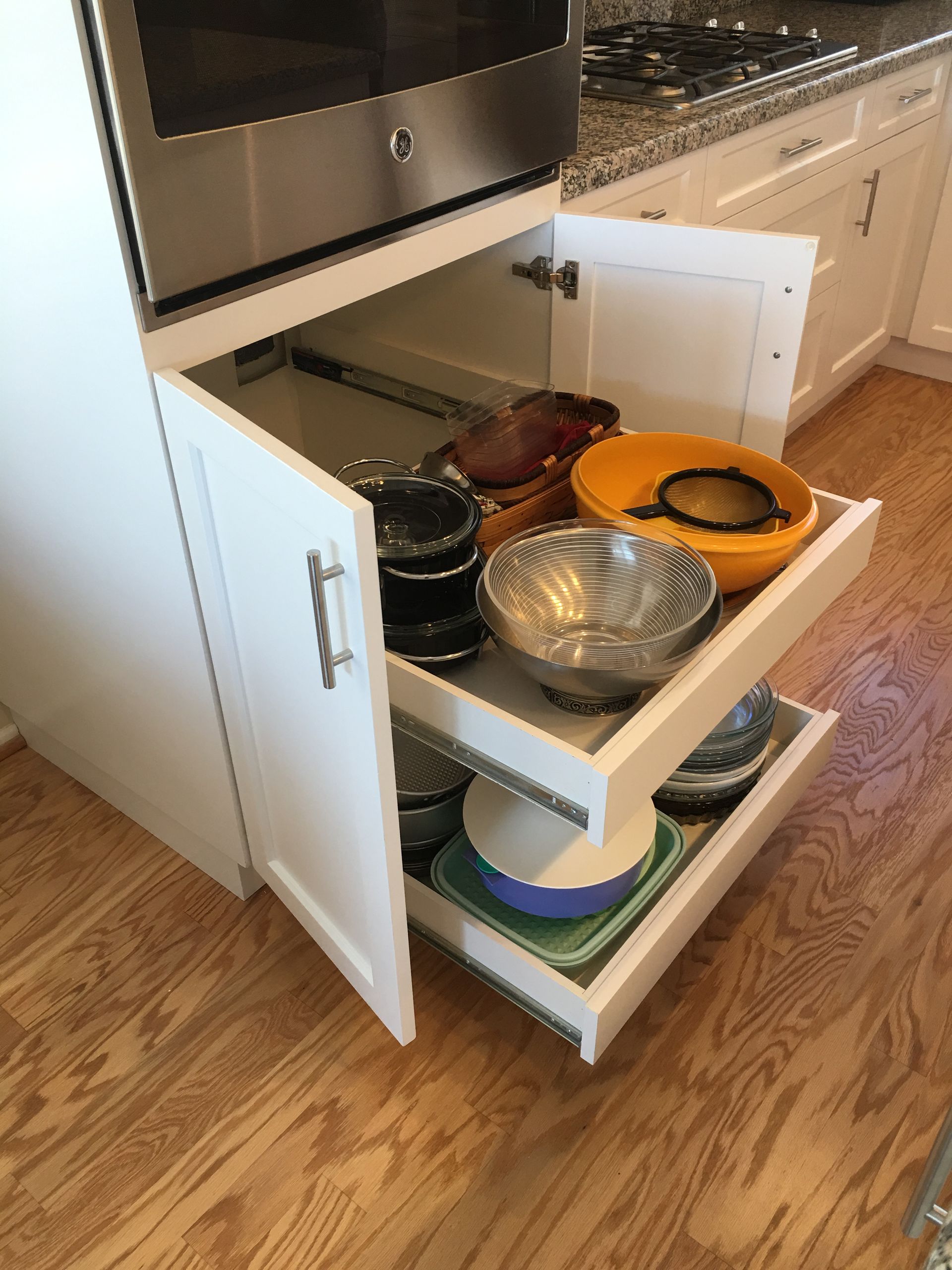 White kitchen cabinet with pull-out drawers holding bowls and cookware, below a microwave.