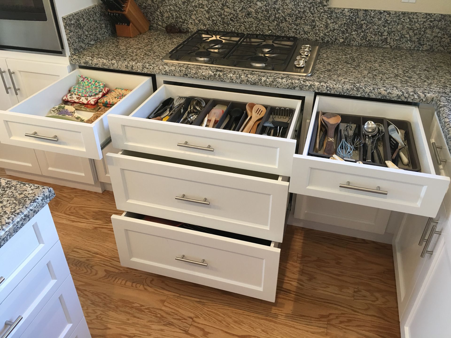 White kitchen drawers open, showing utensils, dish towels, and countertops.