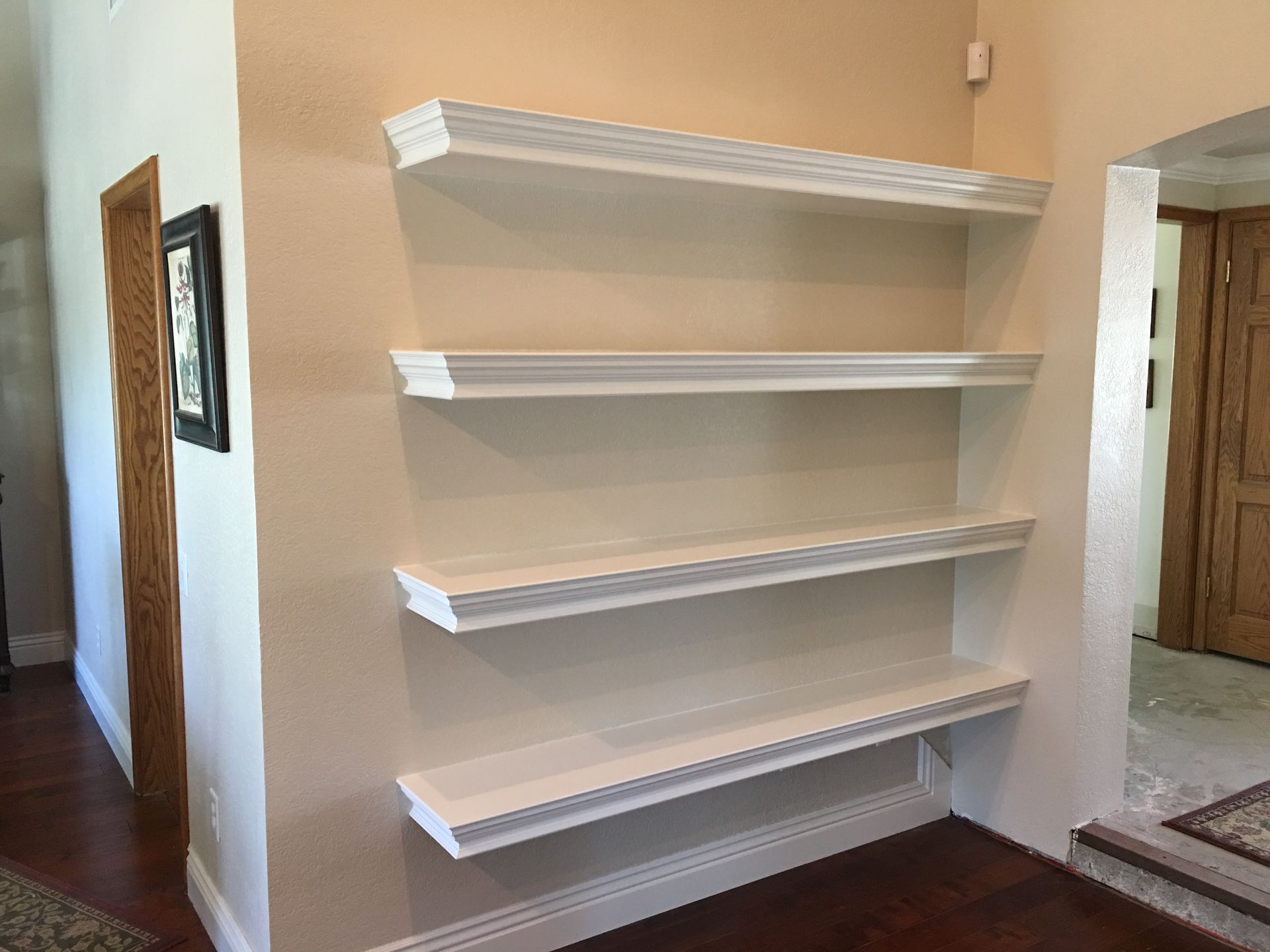 White built-in shelves on a beige wall with wood flooring.