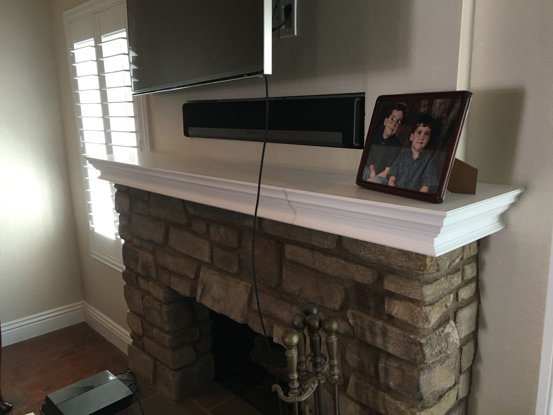 Fireplace with stone facade, white mantel, and TV above. Photo of two people on the mantel.