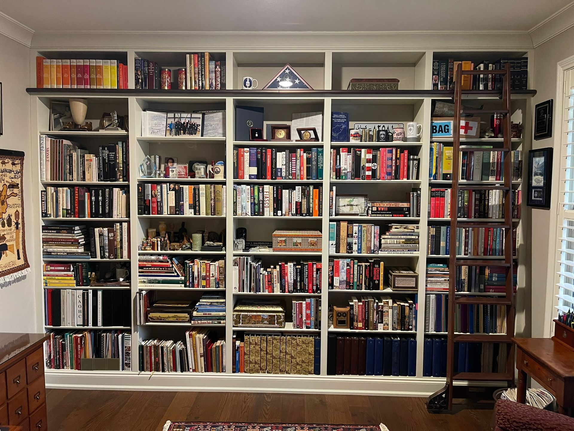 Built-in bookshelf filled with books, decor, and a rolling library ladder in a home setting.