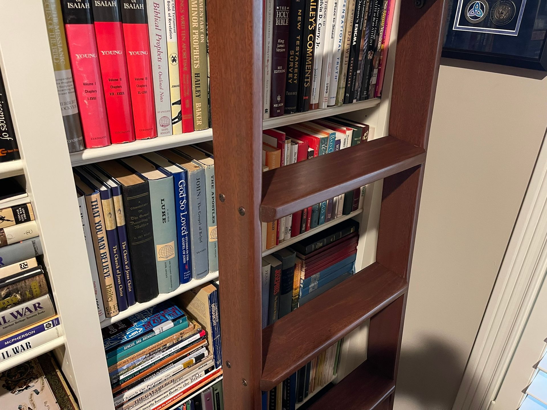 Bookshelves filled with books, some red-spined. Wooden bookshelf frame. Well-lit room.