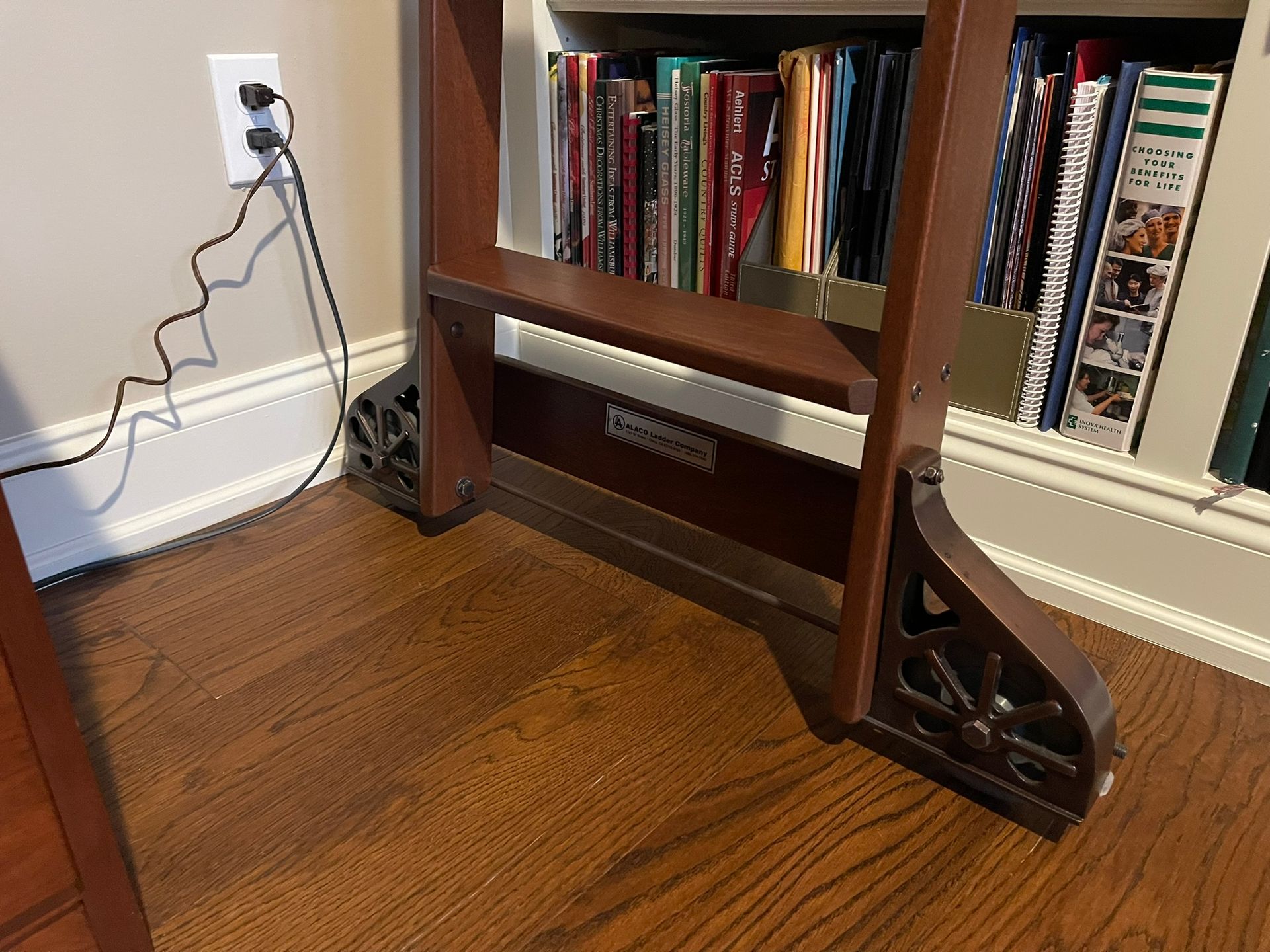 Wooden bookshelf with books, power cord plugged into wall outlet.
