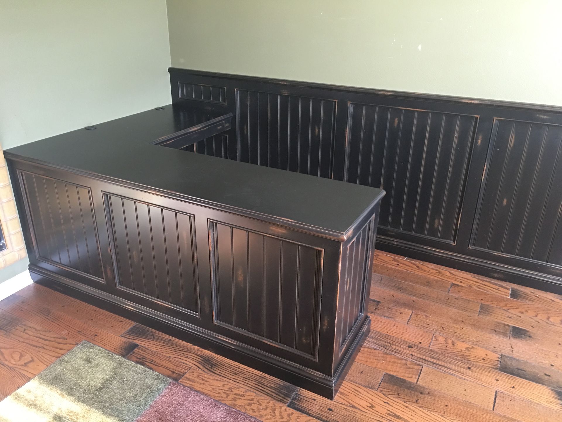 Black L-shaped desk with matching wall paneling on a wood floor.