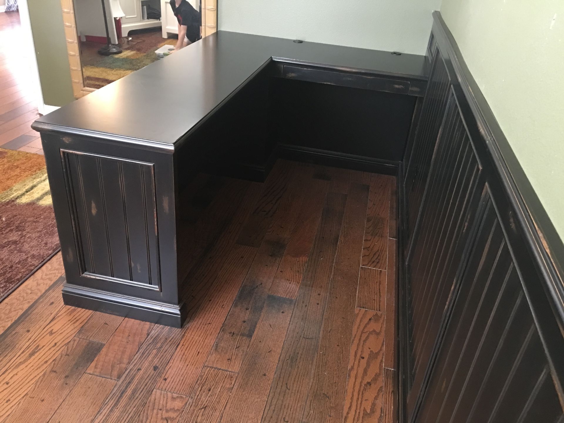 L-shaped black desk against a wall with wooden flooring.