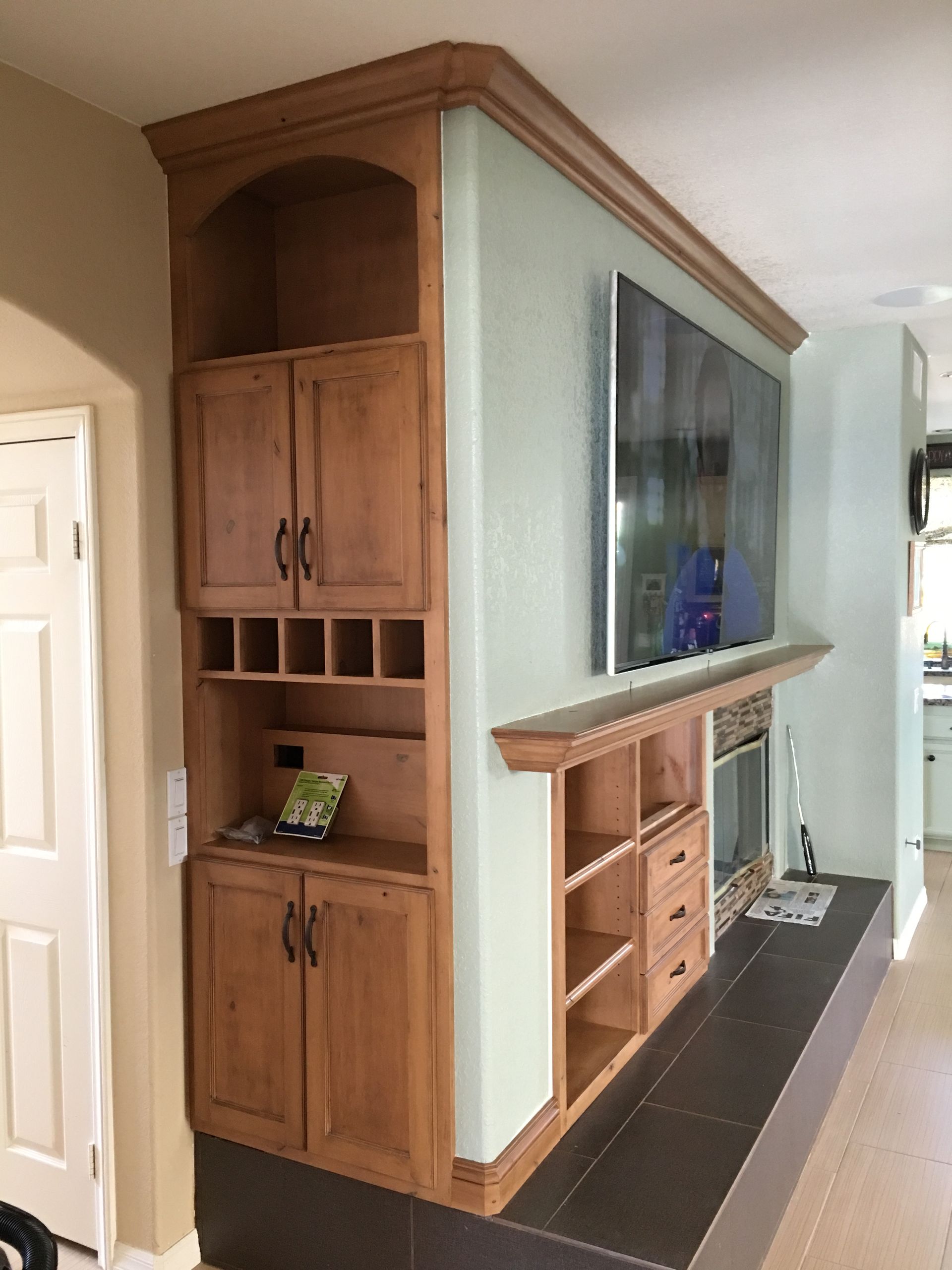 Built-in wooden cabinet with shelves, doors, and a wine rack, next to a fireplace and a mounted TV.