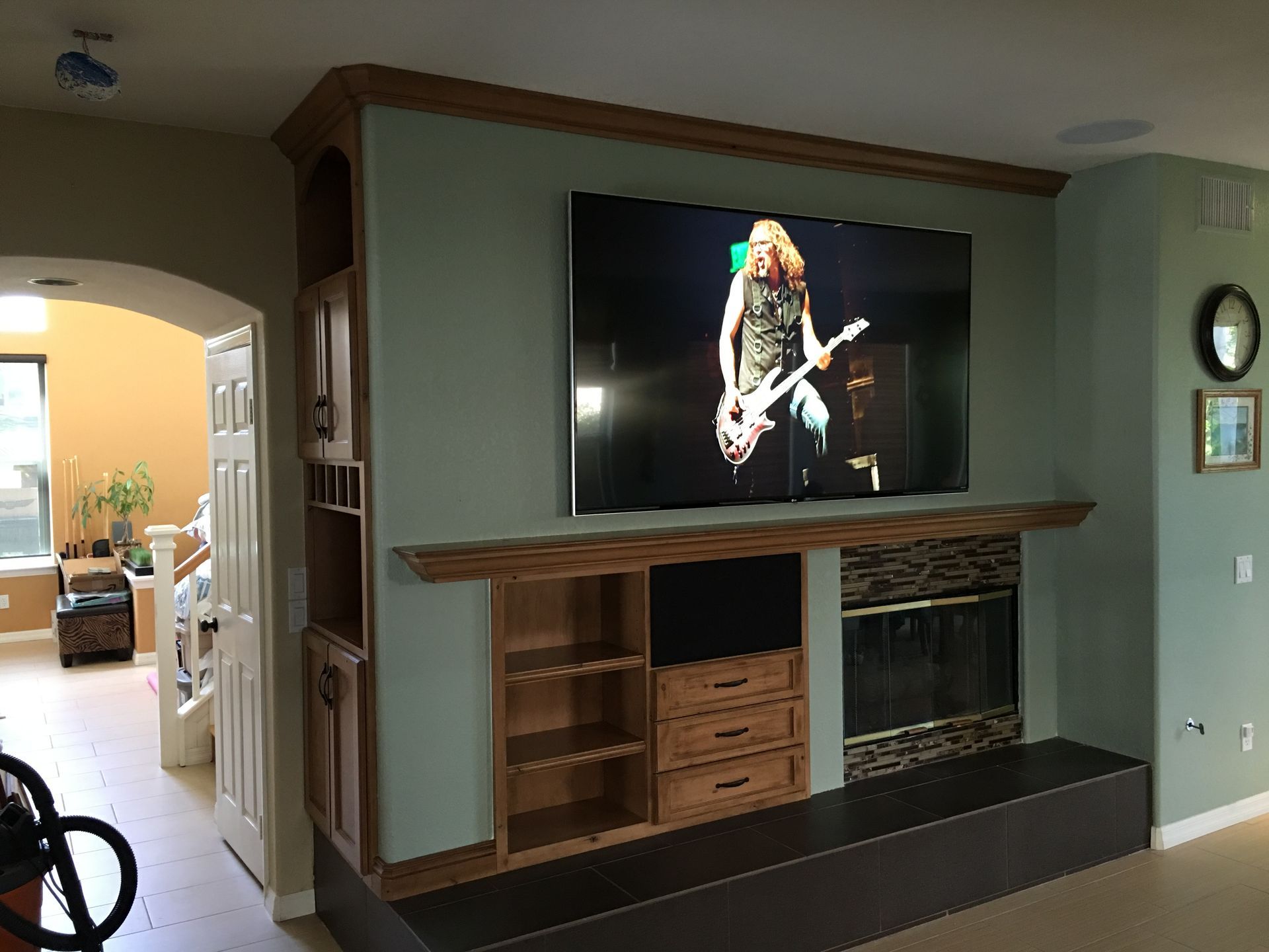 Large TV mounted above a fireplace, built-in shelving, light green wall, and a person playing a guitar on the screen.