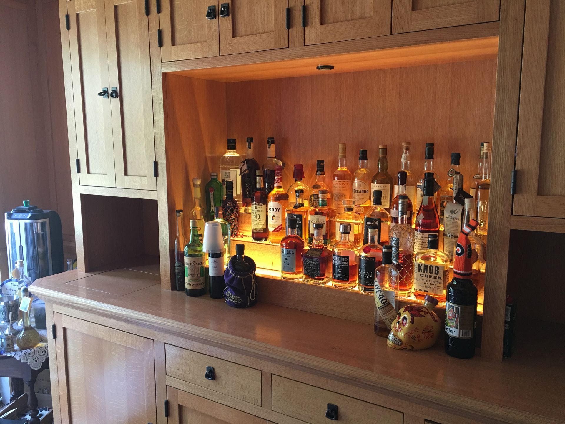 Wooden home bar with lit liquor bottles.