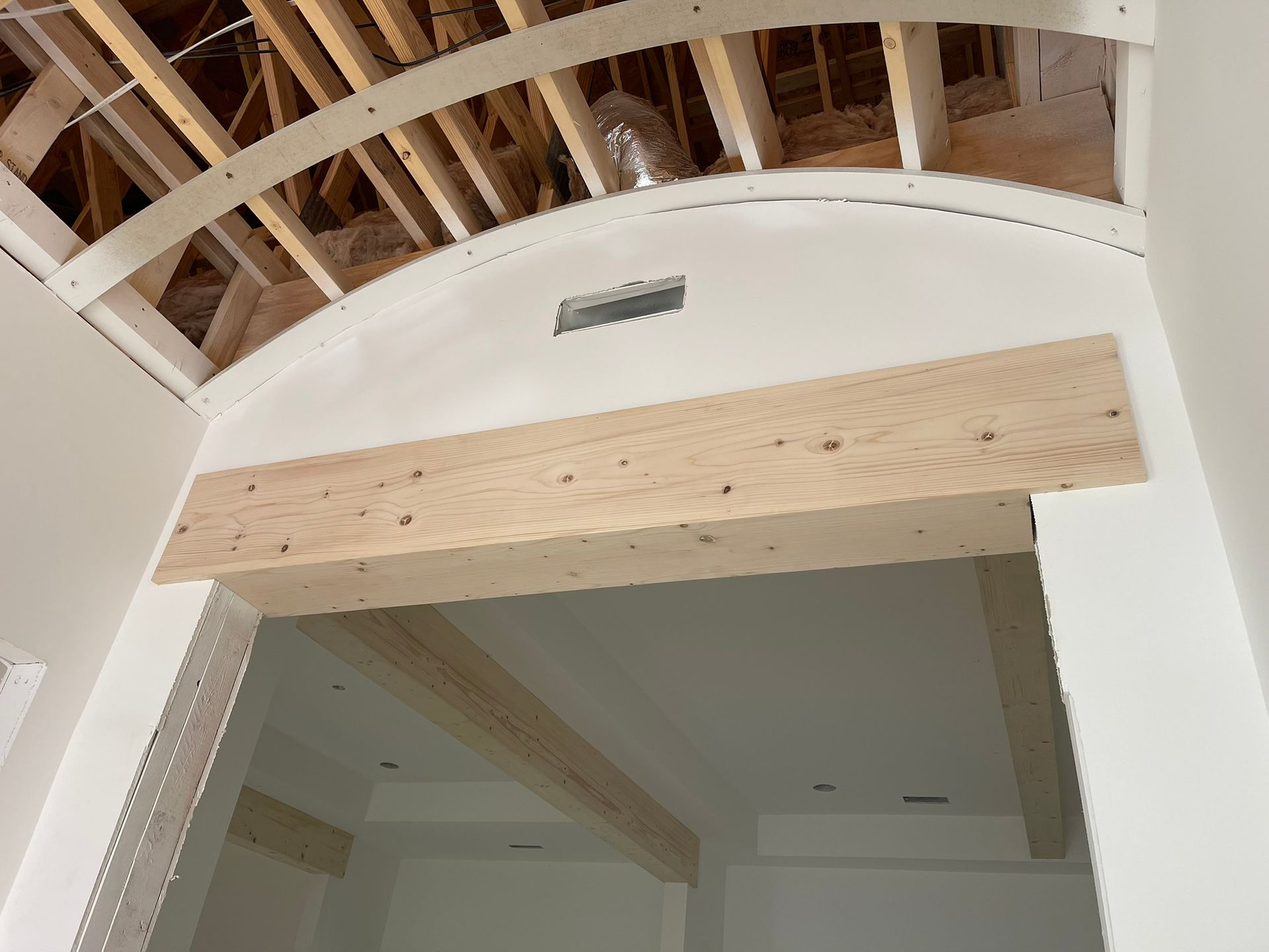 Interior construction: arched doorway with a wooden beam, drywall, and exposed ceiling beams.
