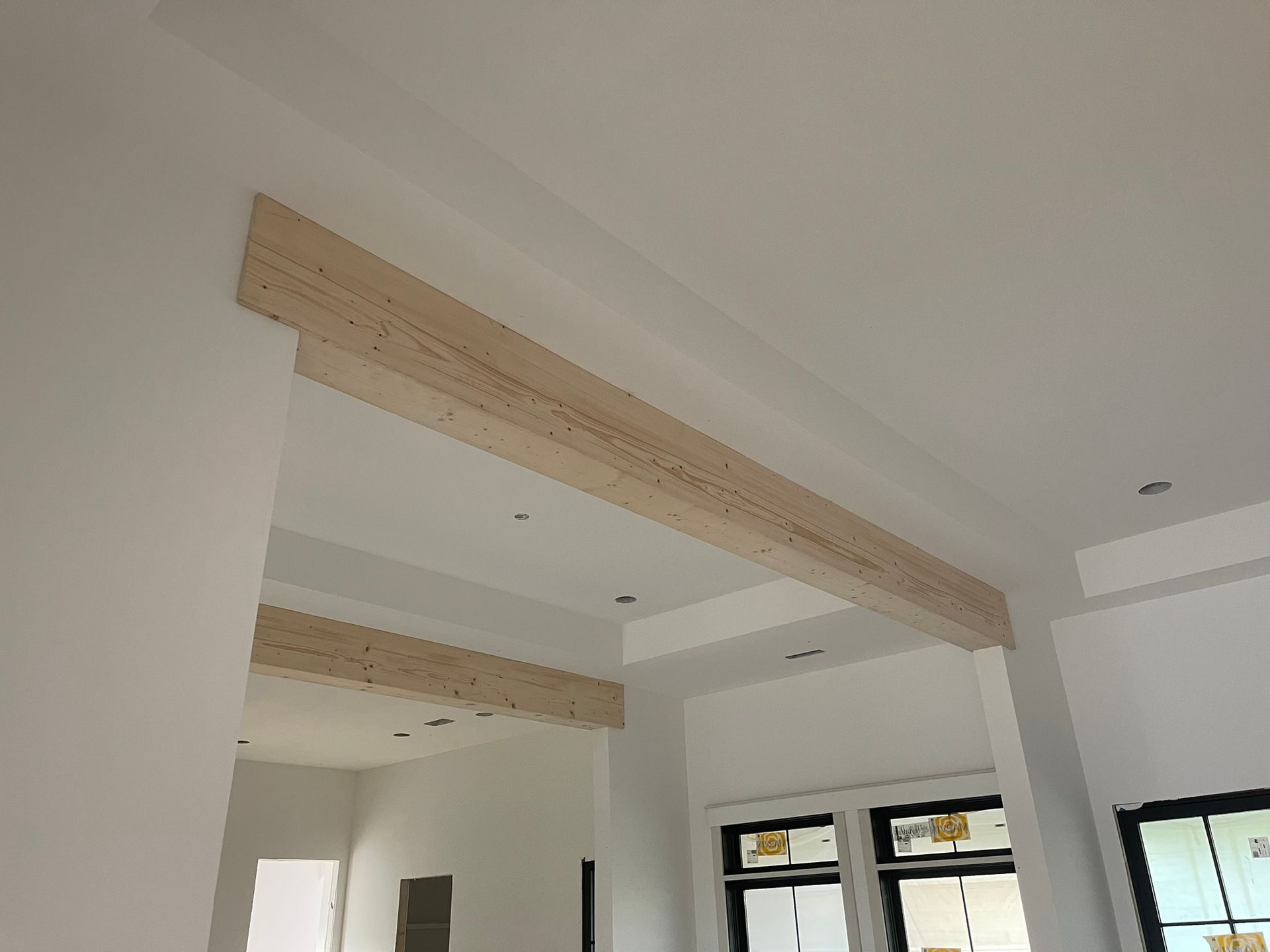 Interior view of a room with unfinished drywall and wooden beams across the ceiling.