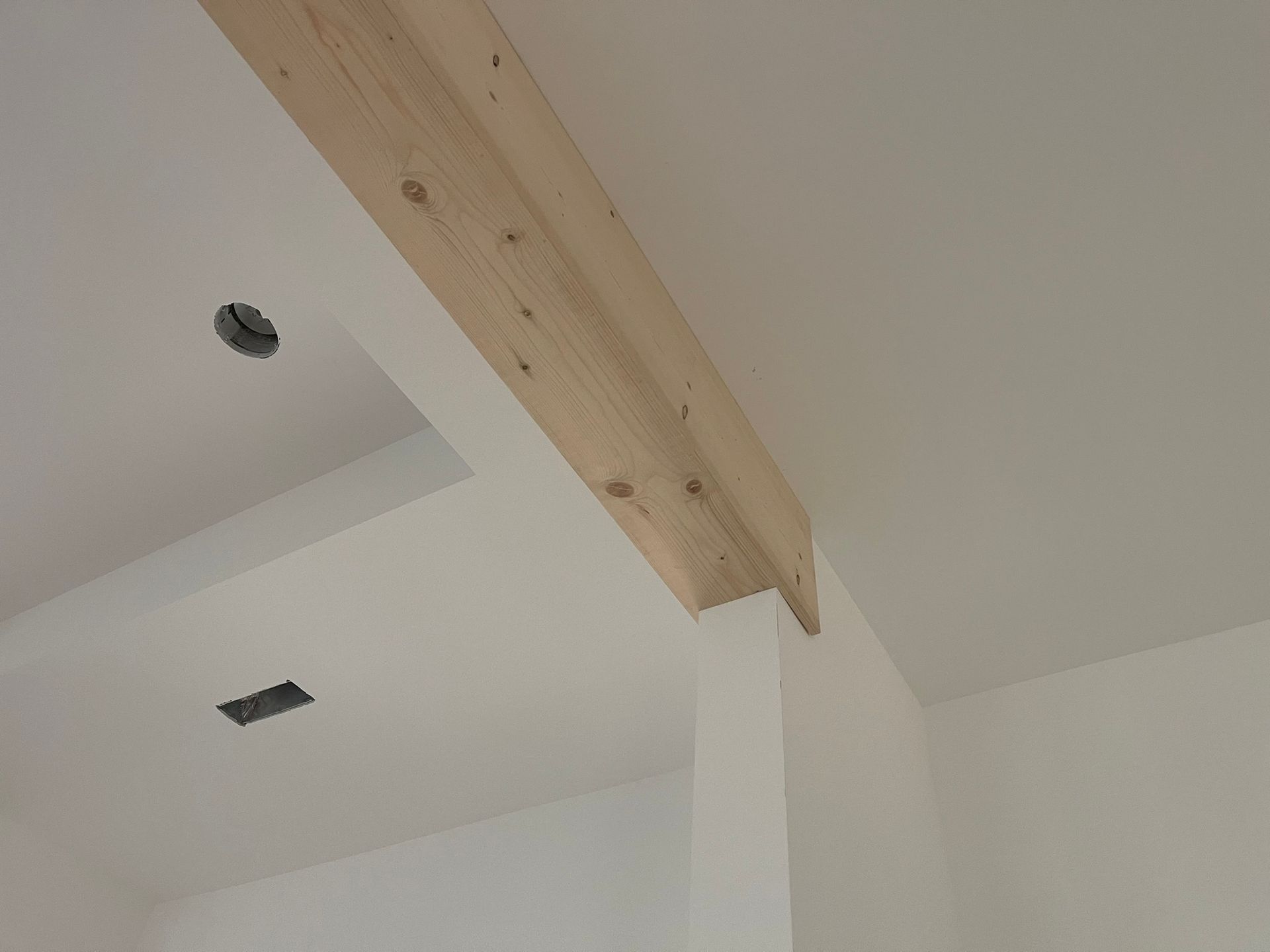 Wooden beam attached to a white wall and ceiling. Electrical box and hole visible in ceiling.