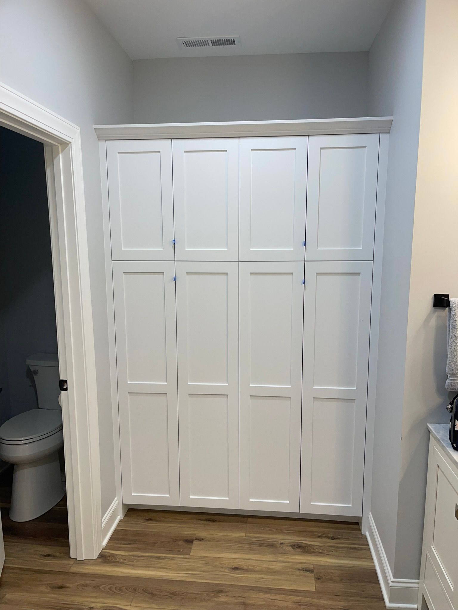 White storage cabinets in a bathroom hallway with an open door to the left, and a sink to the right.