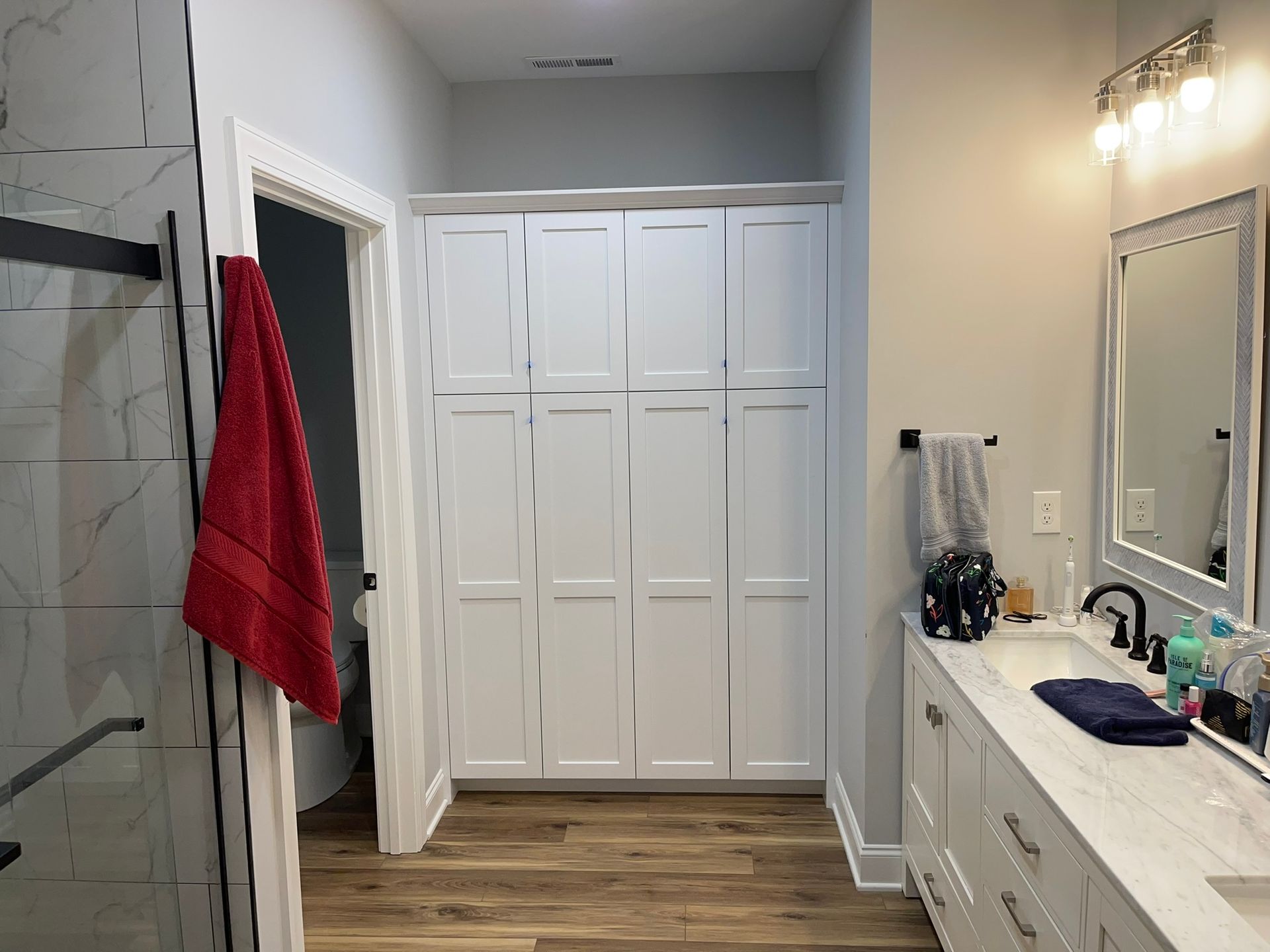 Bathroom with white cabinets, vanity, and shower. A red towel hangs on a door.
