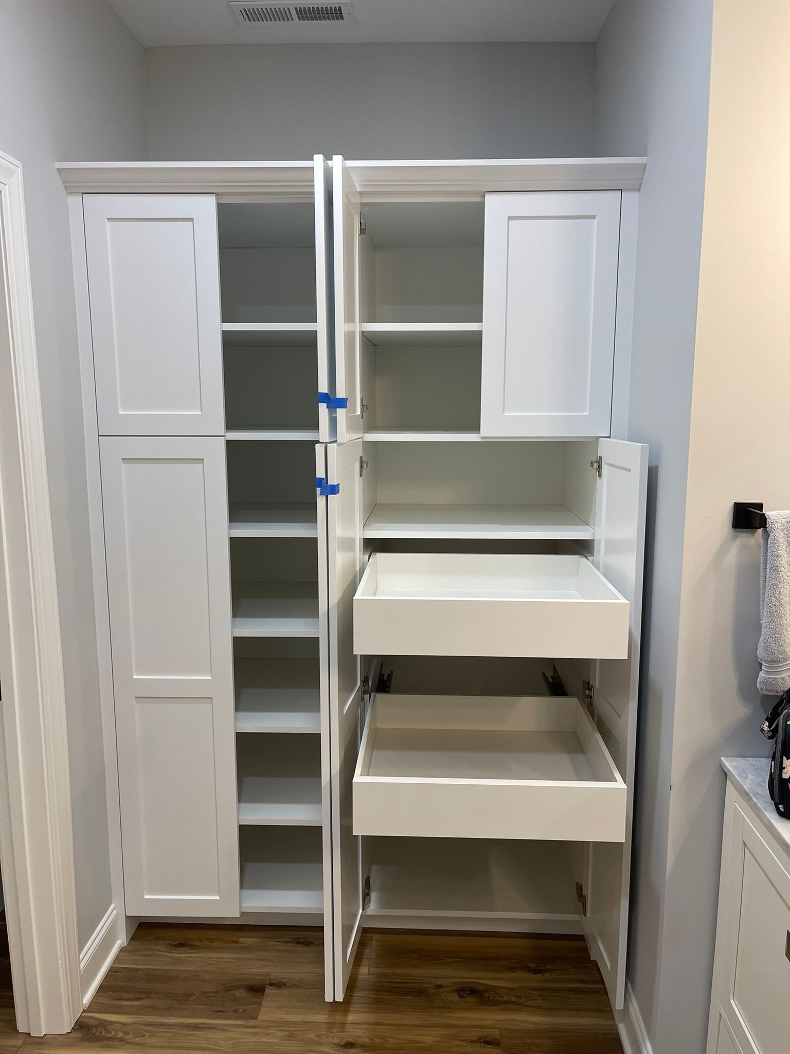 White cabinet with shelves and pull-out drawers, set in a room with hardwood floors.