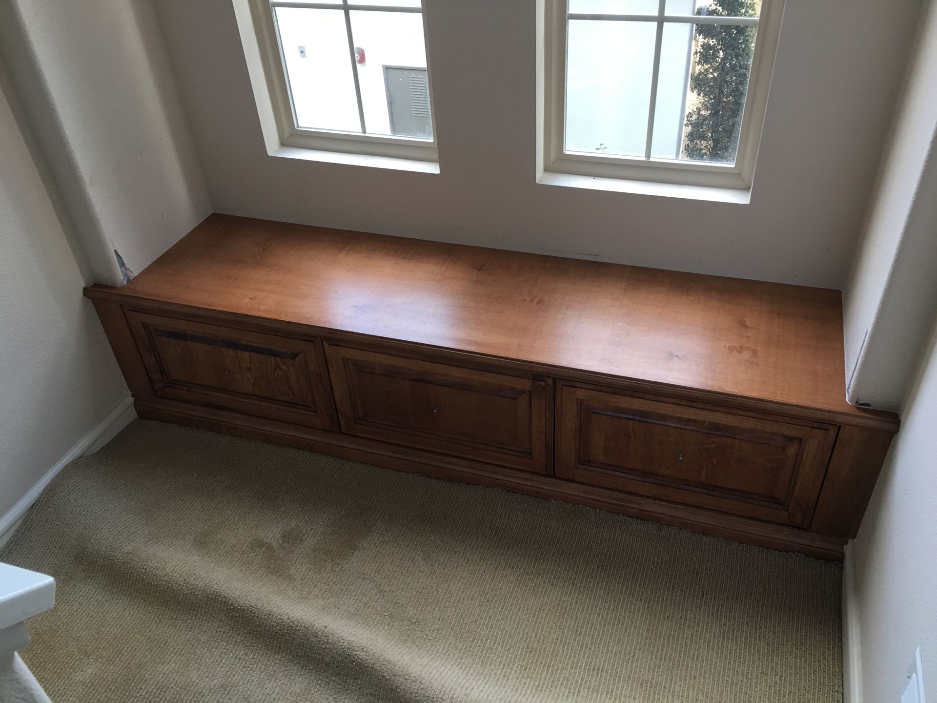 Wooden bench built into alcove, below two windows. Brown, rectangular. Beige carpet.
