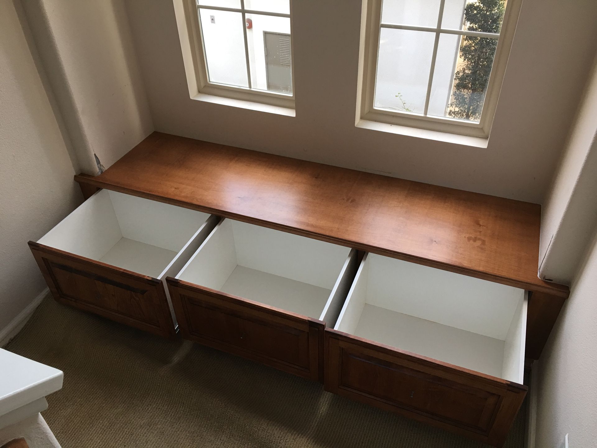Brown wooden bench with three open storage drawers beneath windows.