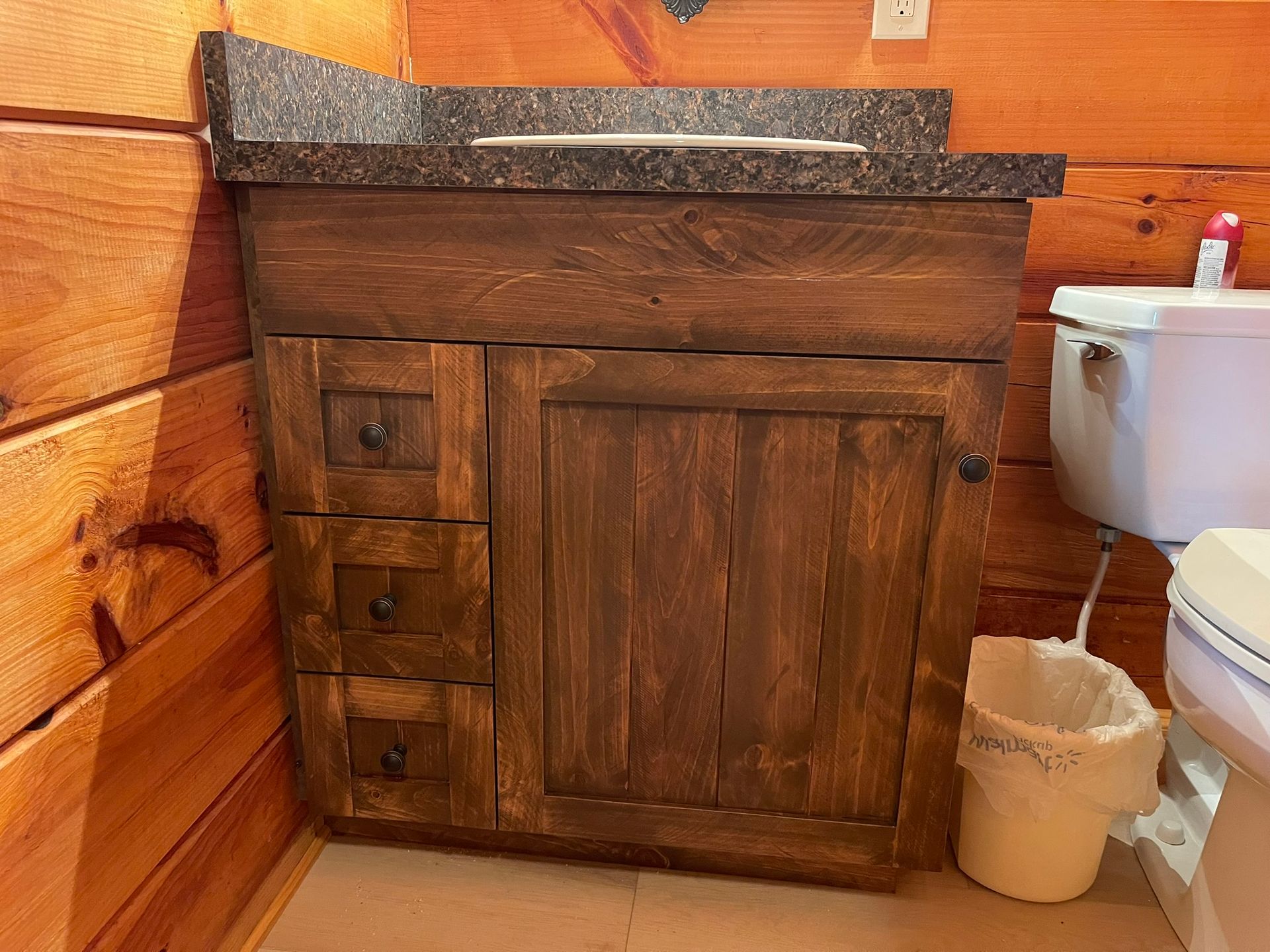 Wooden bathroom vanity with granite countertop and drawers, next to a toilet.
