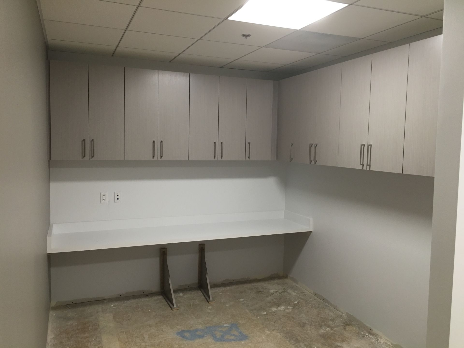Empty gray office space with overhead cabinets and a built-in desk.
