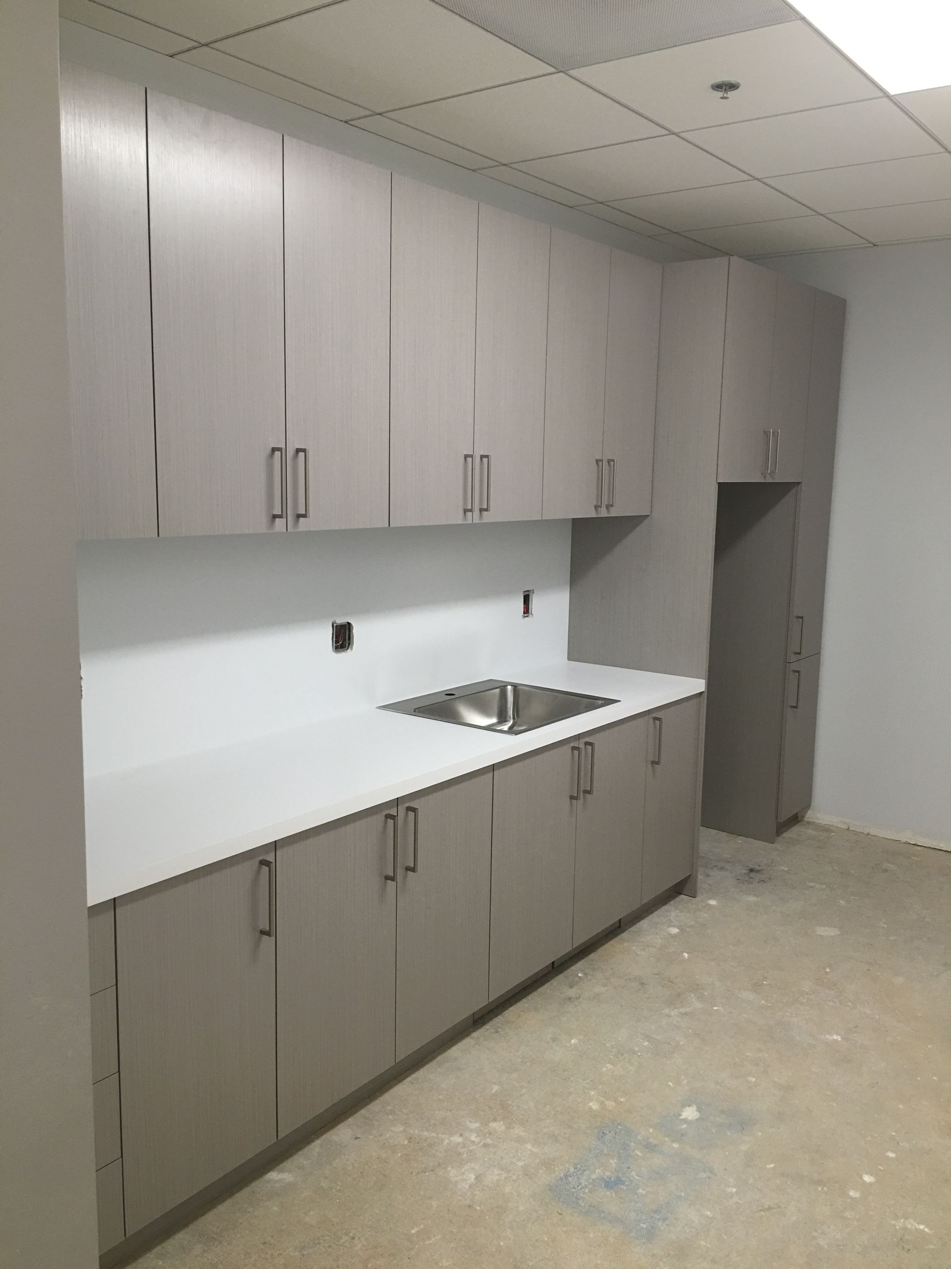 Light gray cabinets with white countertop and sink in a room under construction.