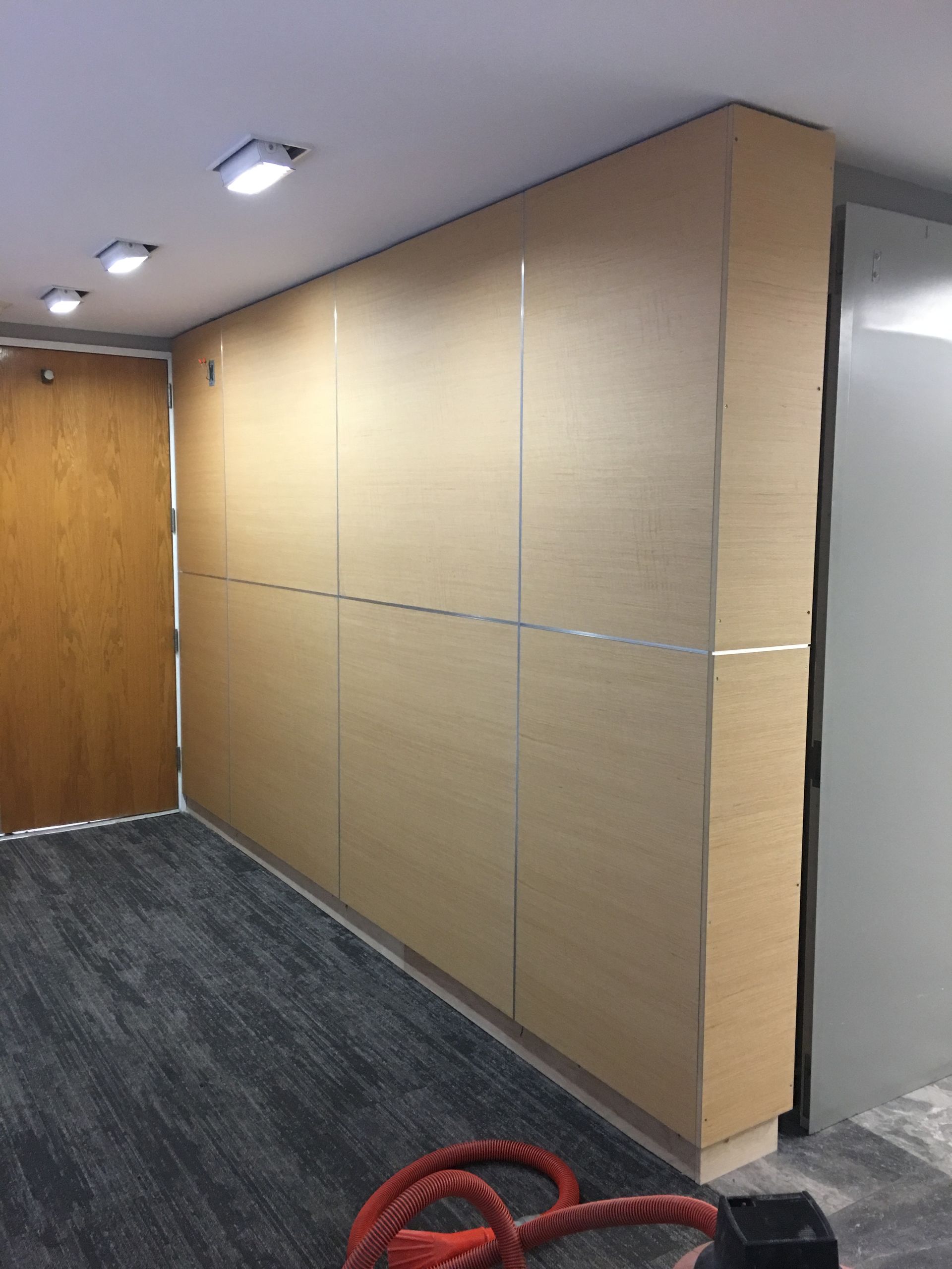 Wooden cabinets and door in an office space with grey carpet.